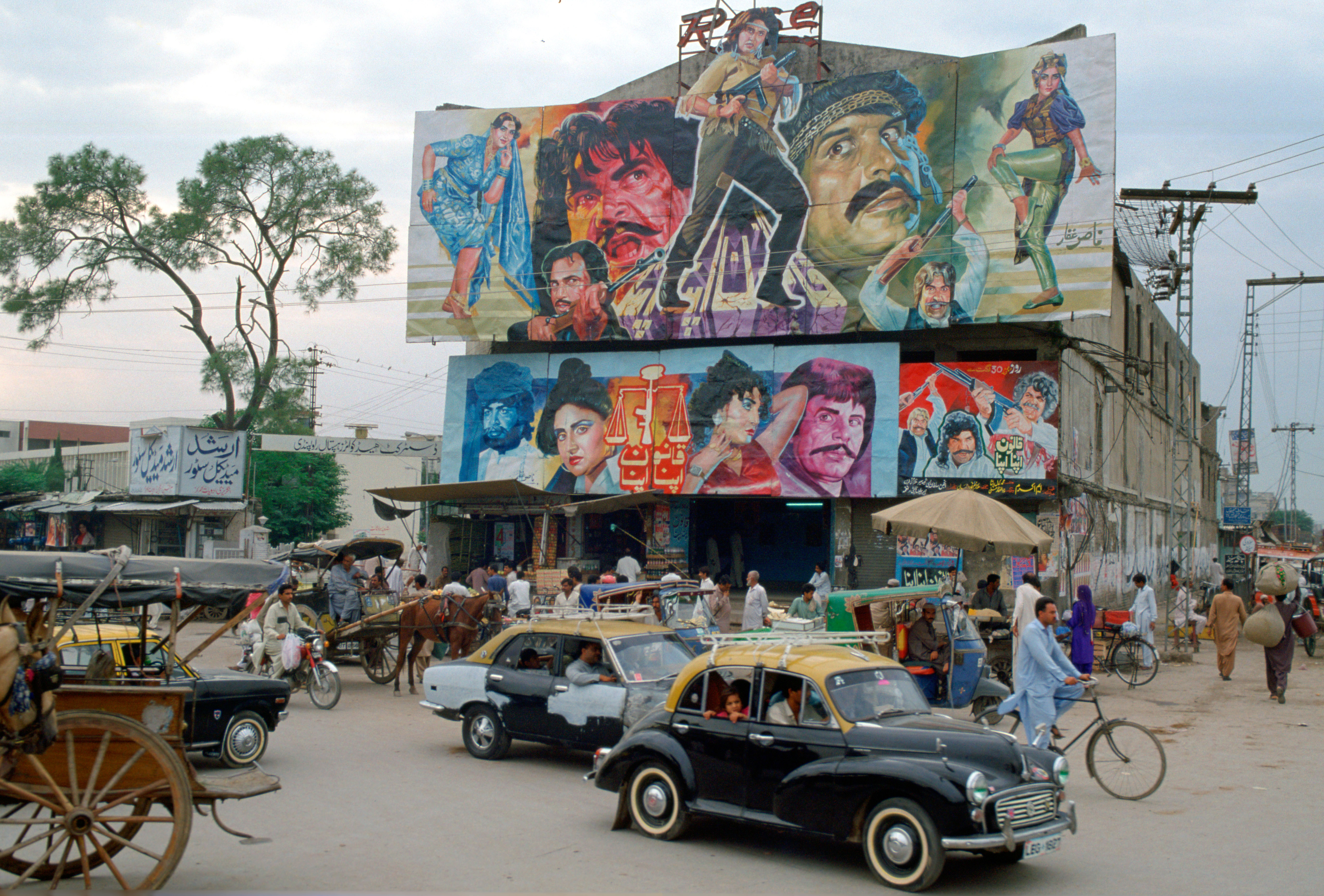 Street scene in Islamabad, Pakistan showing rickshaws, an old two-tone Morris Minor car and the local cinema advertising films often described as "Bollywood'.