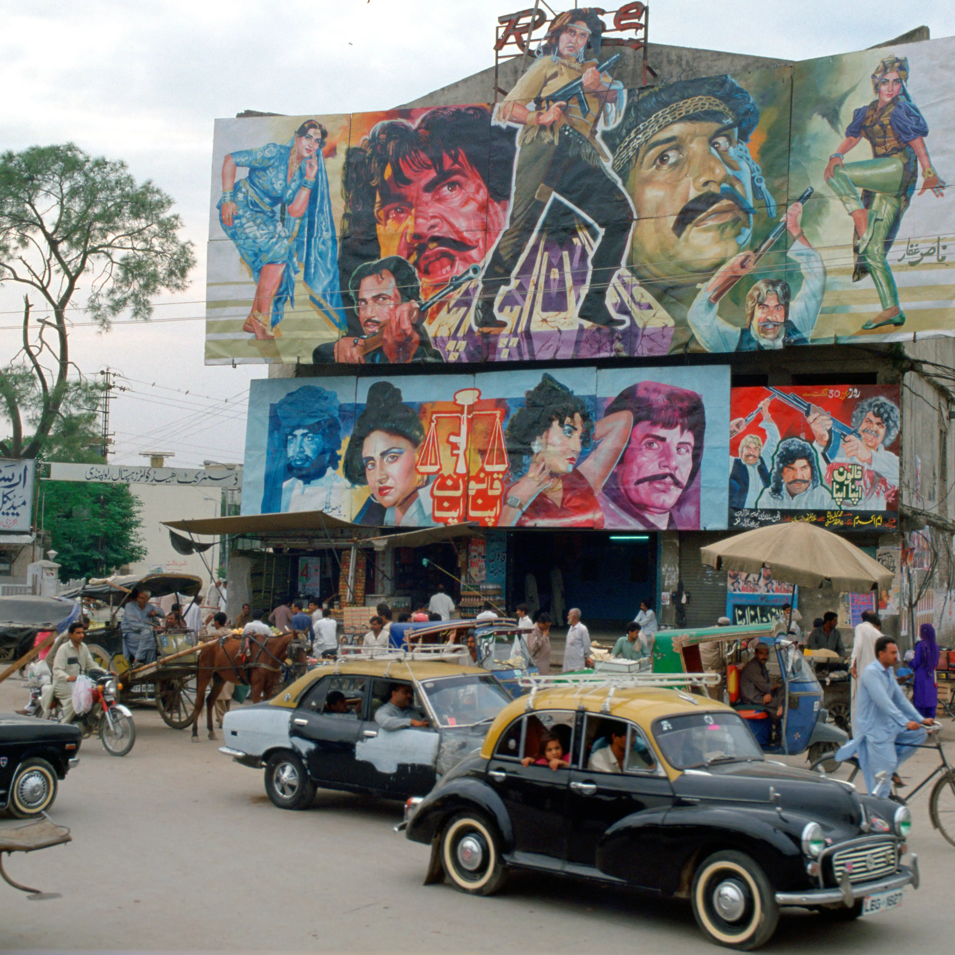 Street scene in Islamabad, Pakistan showing rickshaws, an old two-tone Morris Minor car and the local cinema advertising films often described as "Bollywood'.
