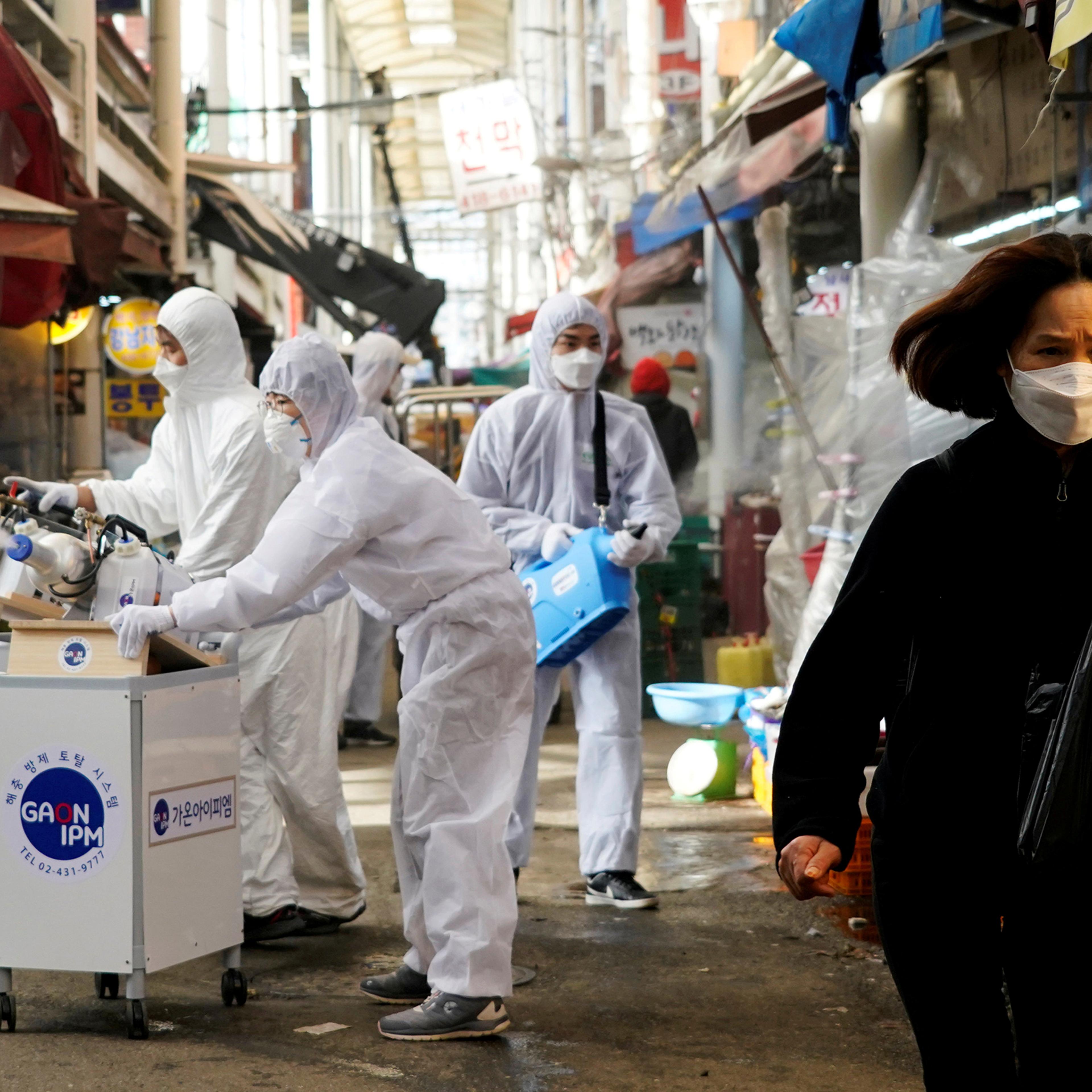 A woman wearing a mask to prevent contracting the coronavirus reacts as employees from a disinfection service company sanitize a traditional market in Seoul