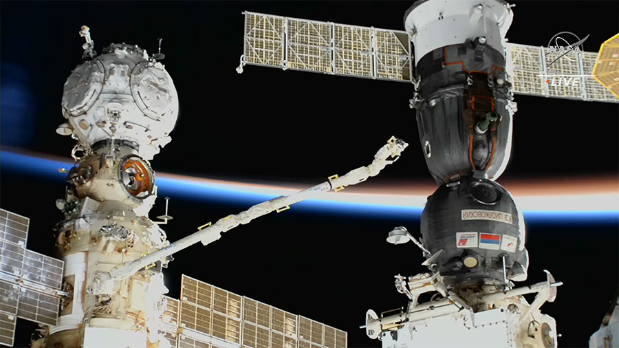A camera at the end of one of the the space station's robotic arms examines the leaking Soyuz (right)