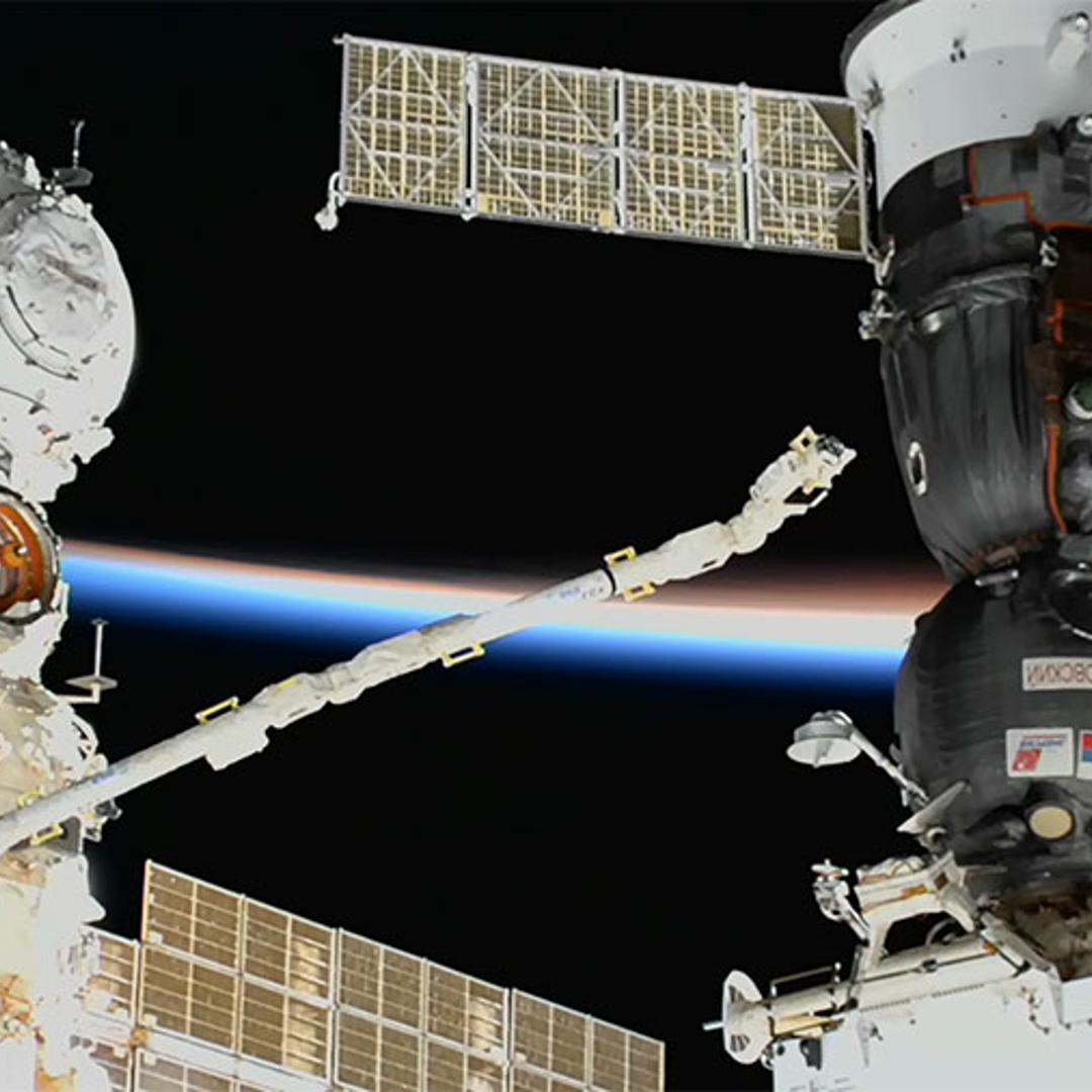 A camera at the end of one of the the space station's robotic arms examines the leaking Soyuz (right)
