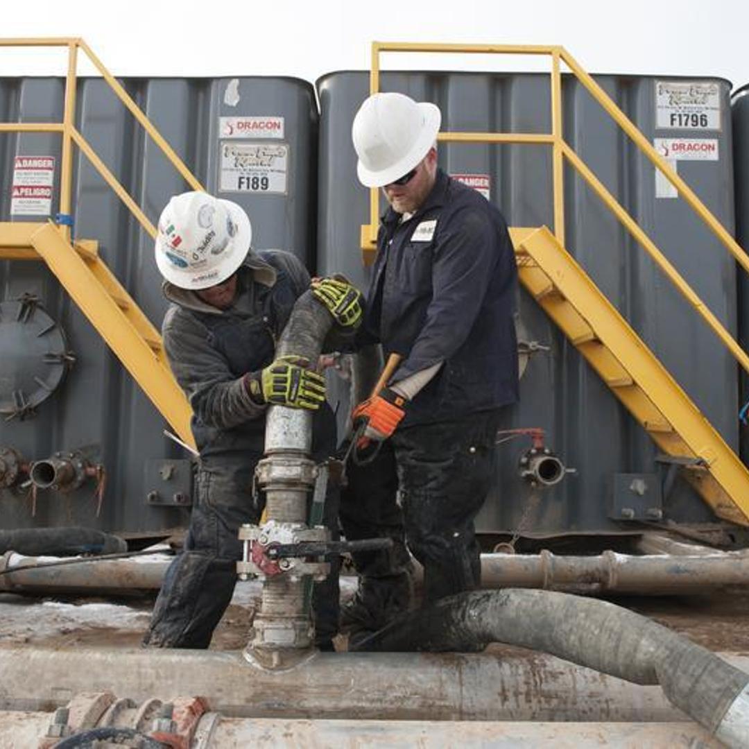 Mody Torres (L) and Josh Anderson of Select Energy Services connect hoses between a pipeline and water tanks at a Hess fracking site near Williston, North Dakota Nov. 12, 2014.