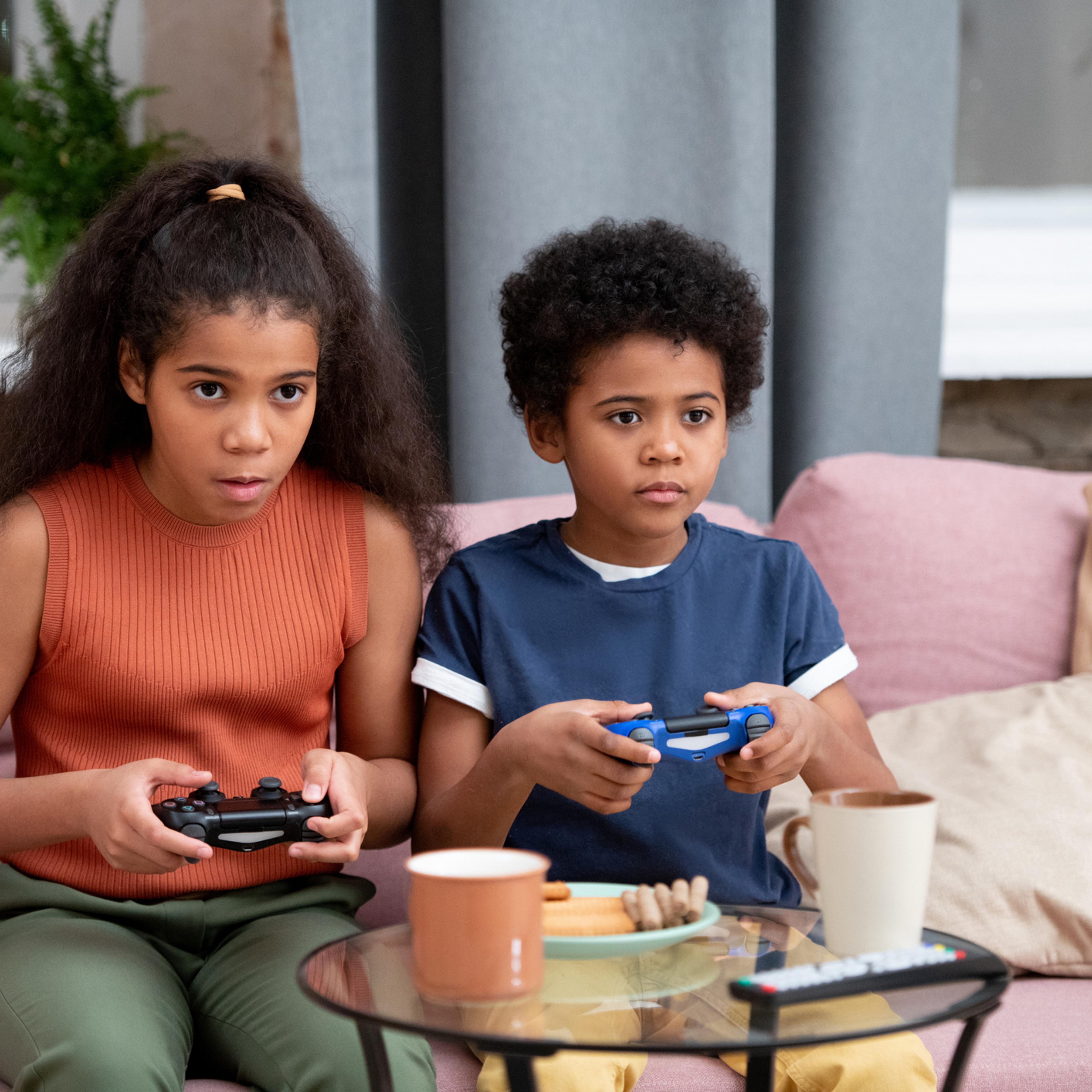 Cute boy and girl of African ethnicity playing video game on couch at home