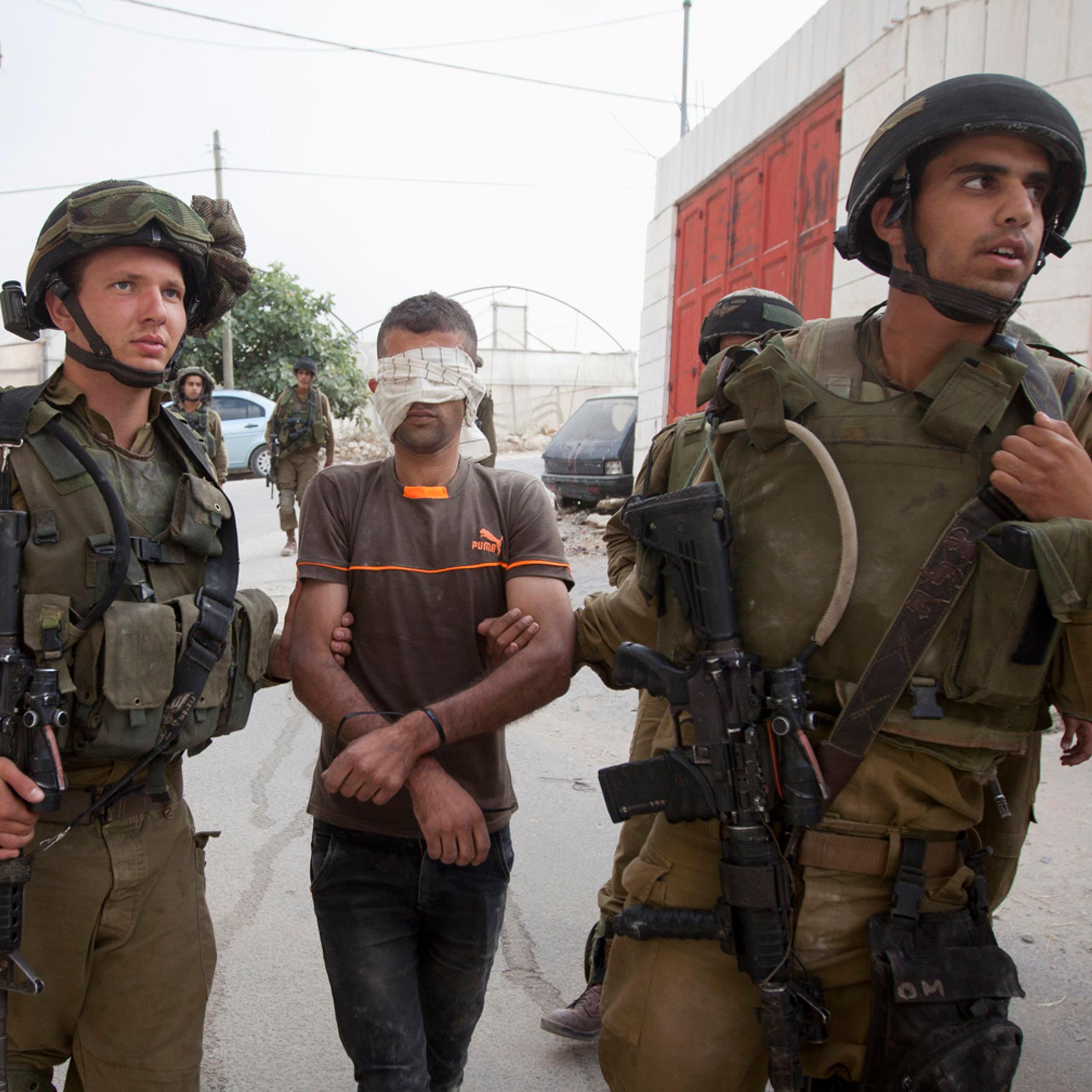 Israeli soldiers arrest a Palestinian man during a search for three missing Israeli teens, feared abducted in the West Bank last week, in the village of Beit Kahil near the West Bank city of Hebron on June 21, 2014.