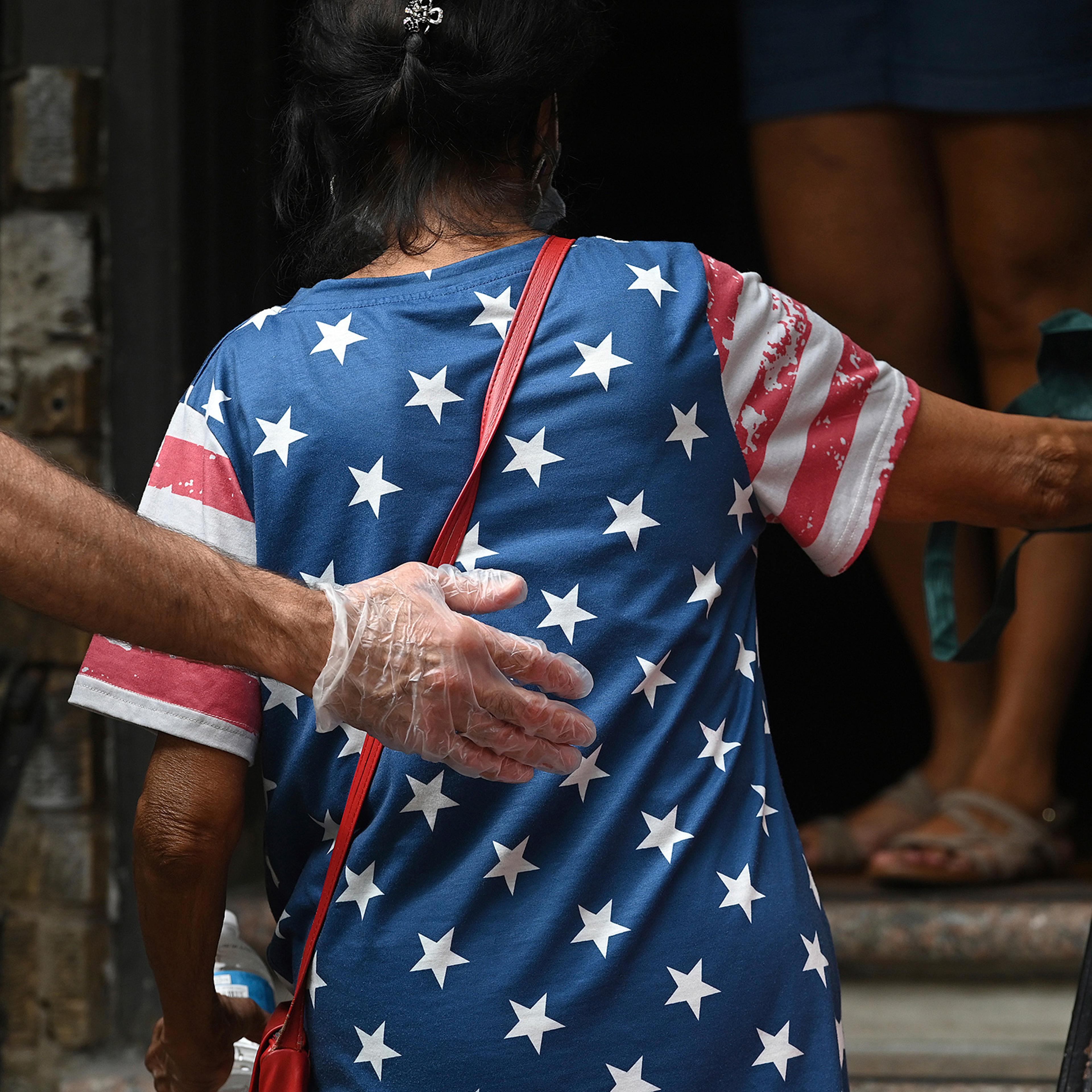 With an outstretched gloved hand, a volunteer helps a woman up the steps of the Mosaic Community Center Food Pantry to receive donated food in Queens on July 31