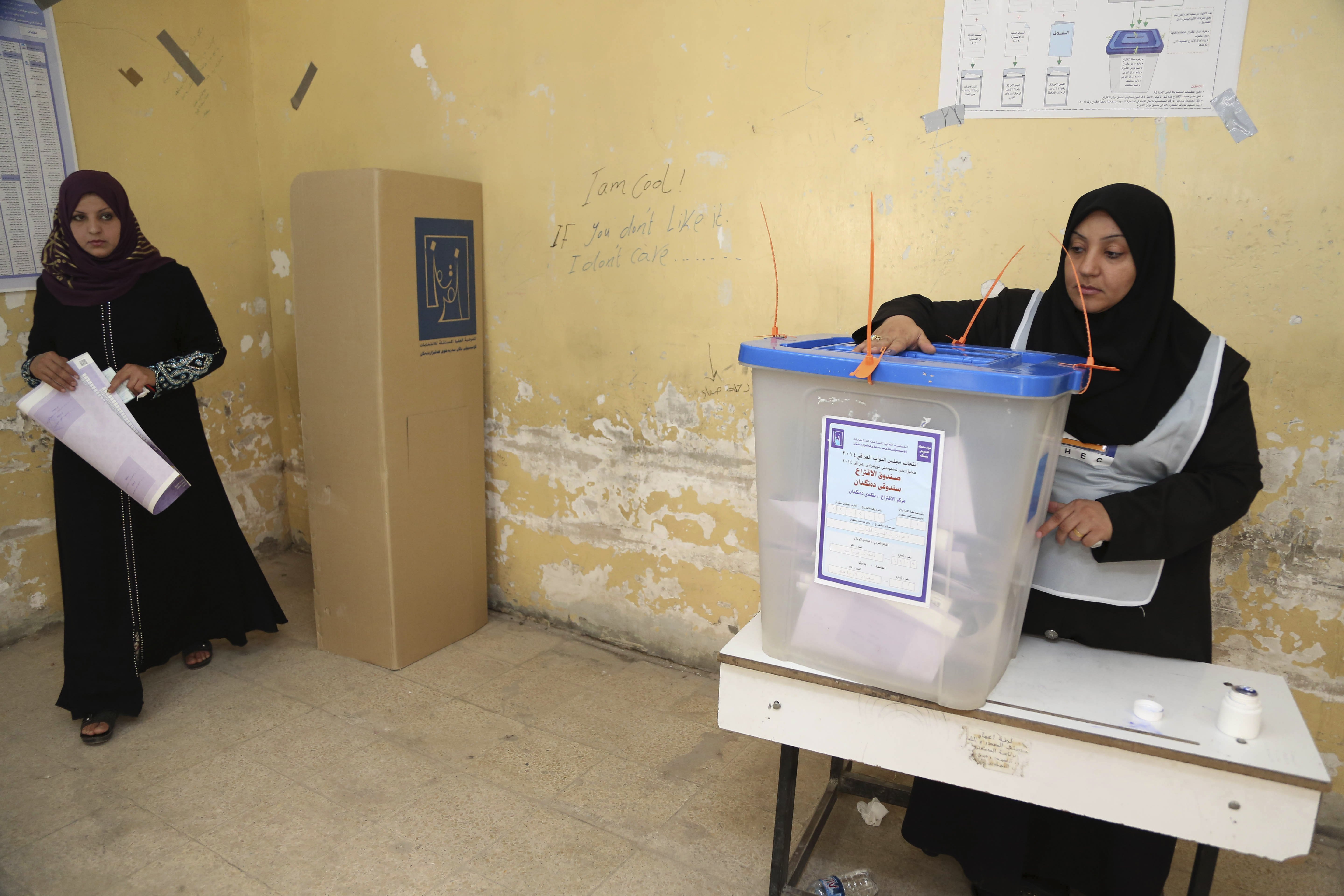 An Iraqi woman, left, prepares to cast her vote at a polling station for parliamentary elections in Baghdad, Iraq, on April 30, 2014.