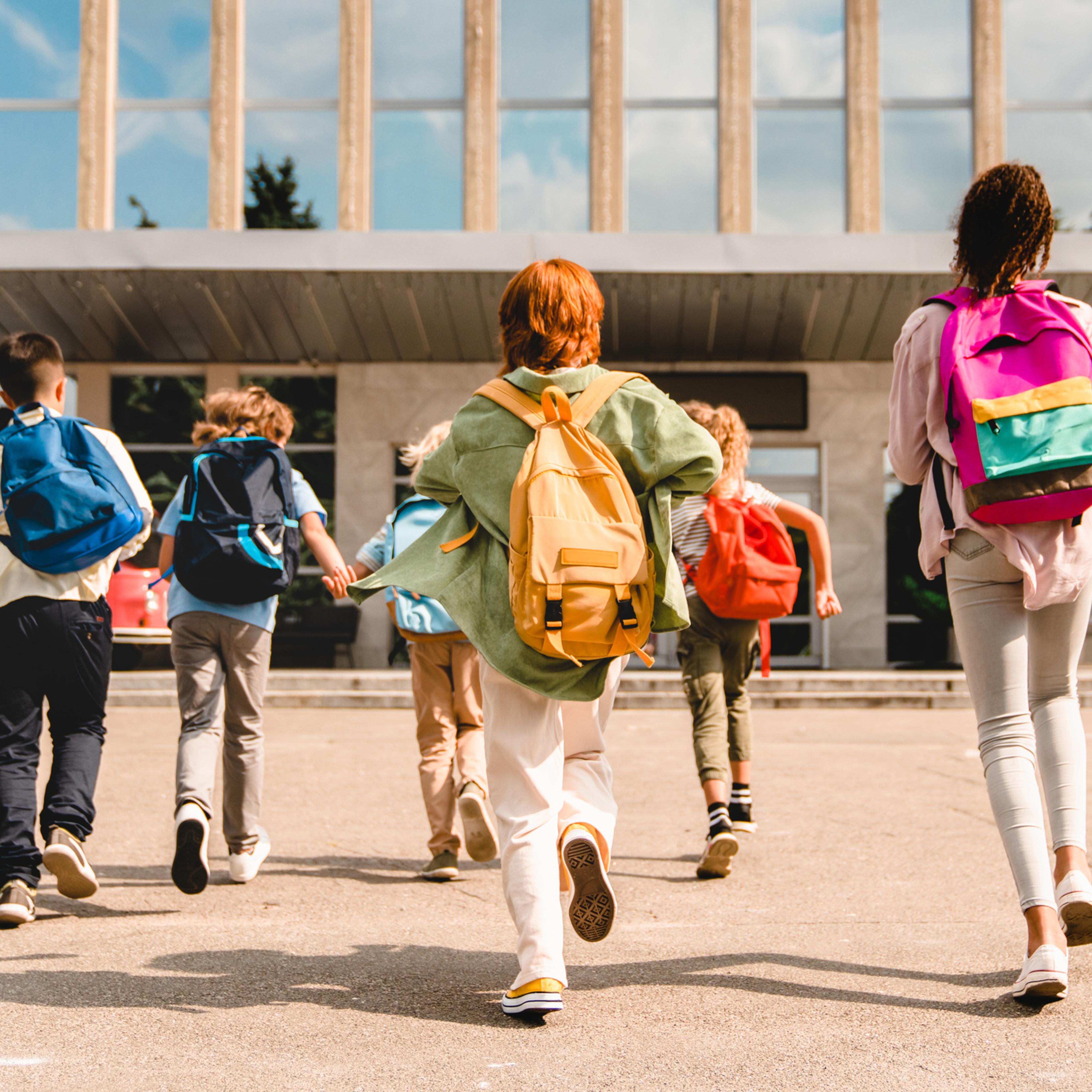 Little kids schoolchildren pupils students running hurrying to the school building for classes lessons from to the school bus. Welcome back to school. The new academic semester year start
