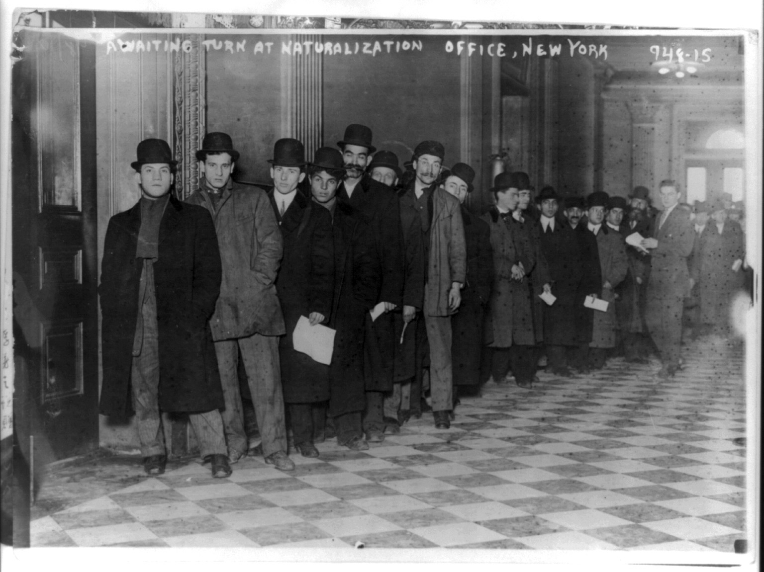 Men standing in line in corridor of naturalization office in New York City, circa 1916.