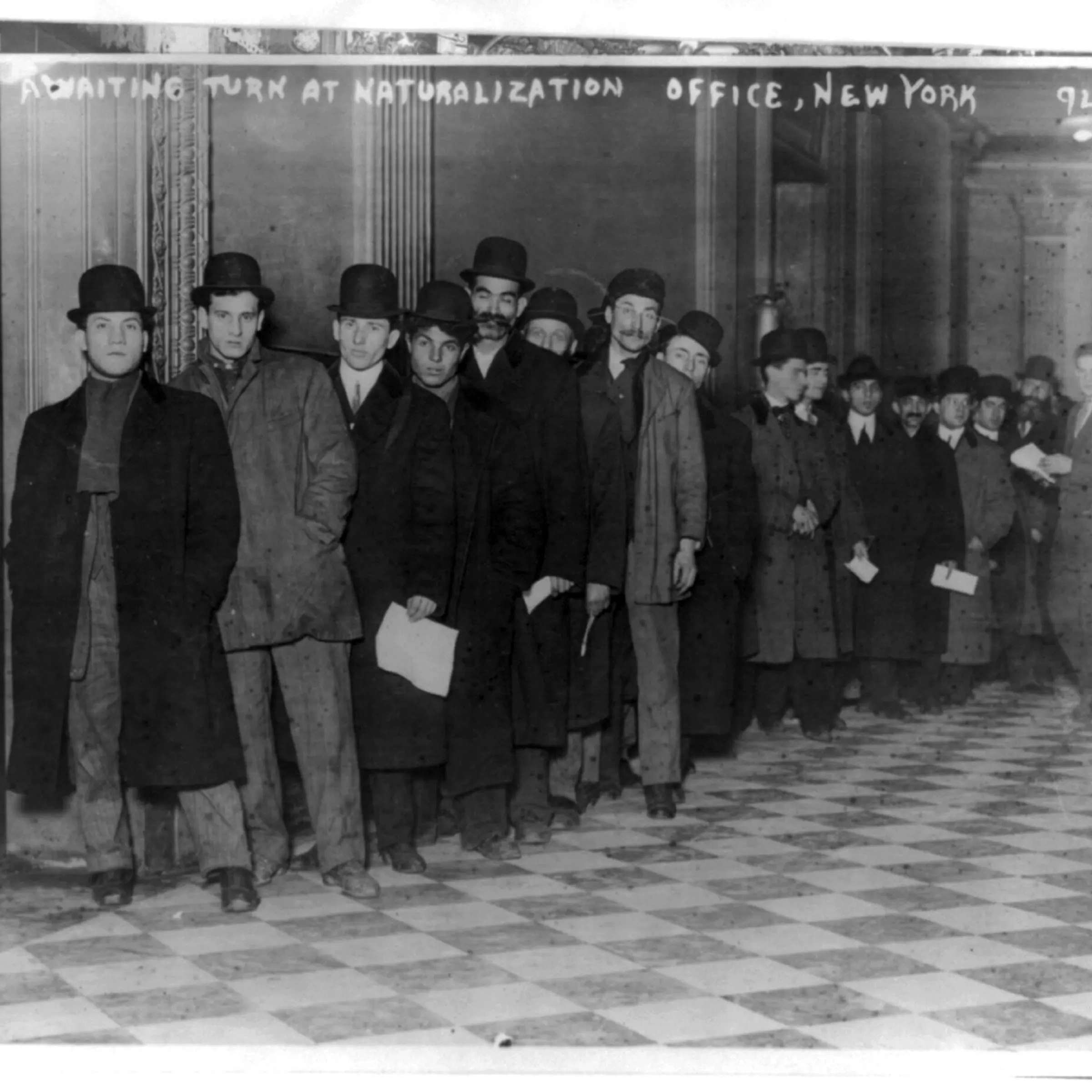 Men standing in line in corridor of naturalization office in New York City, circa 1916.