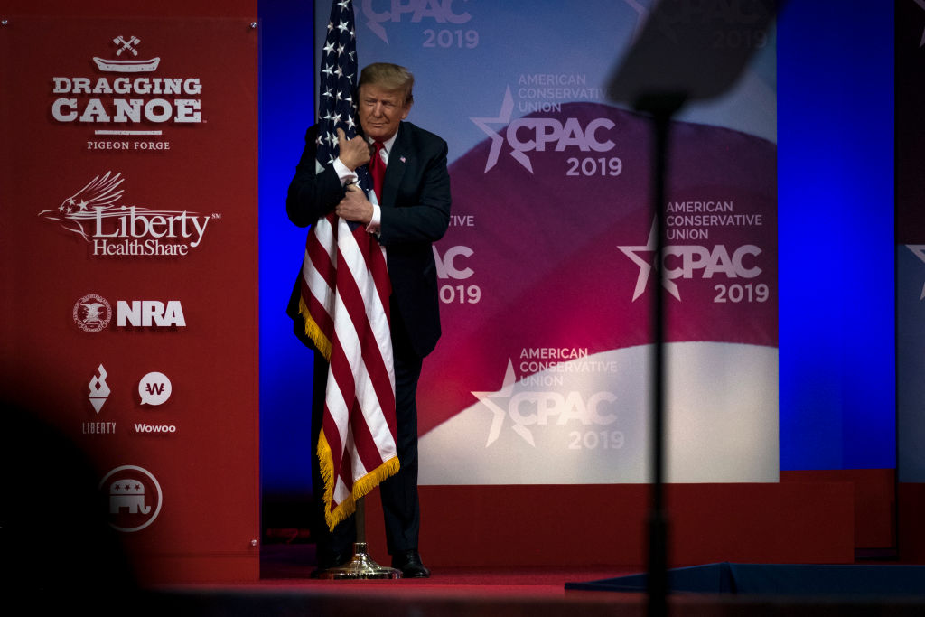 U.S. President Donald Trump hugs a U.S. flag as he takes the stage at CPAC in National Harbor, Maryland