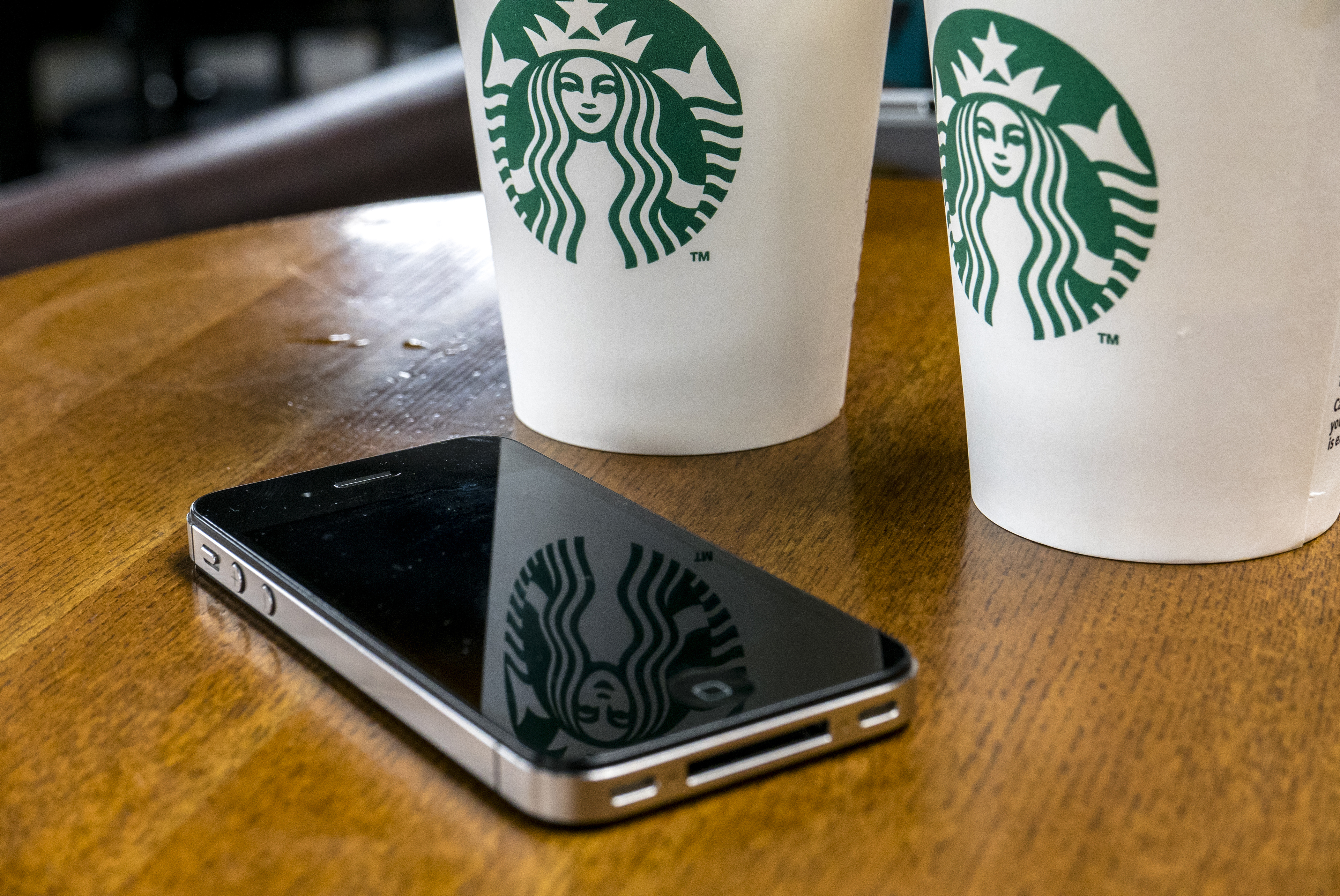 A mobile phone is placed beside coffee cups in a Starbucks