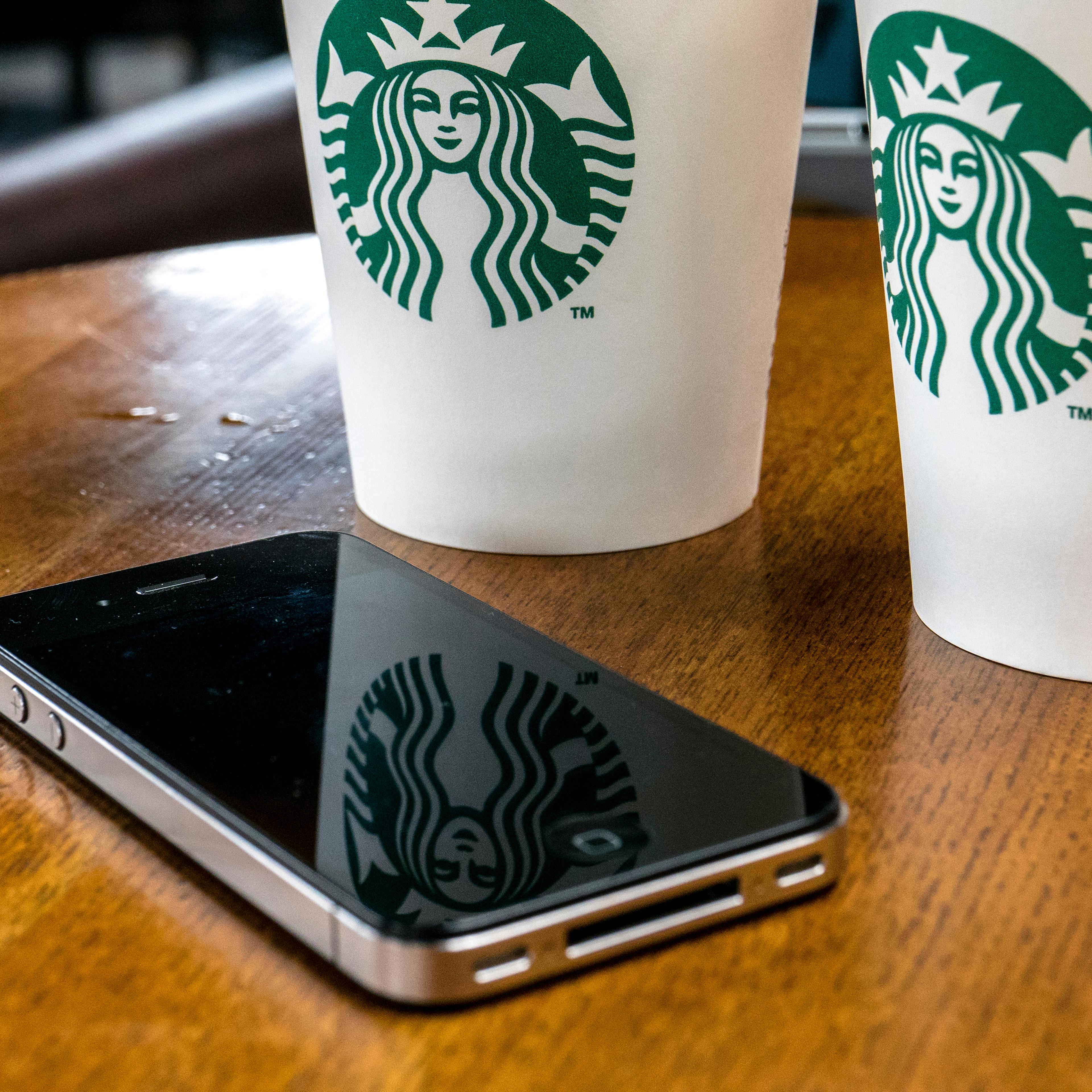 A mobile phone is placed beside coffee cups in a Starbucks