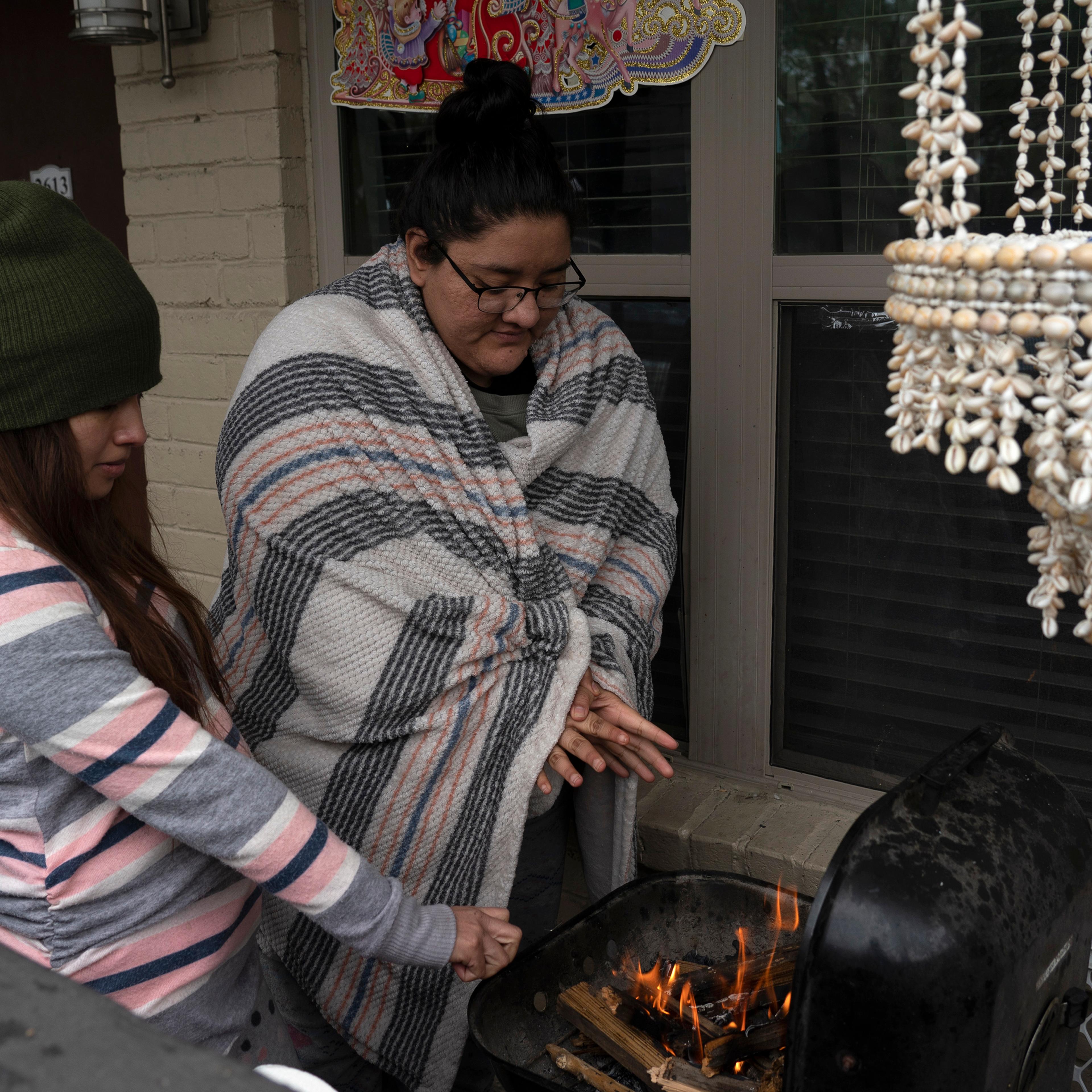 Karla Perez and Esperanza Gonzalez warm up by a barbecue grill during power outage caused by the winter storm on February 16, 2021 in Houston, Texas.