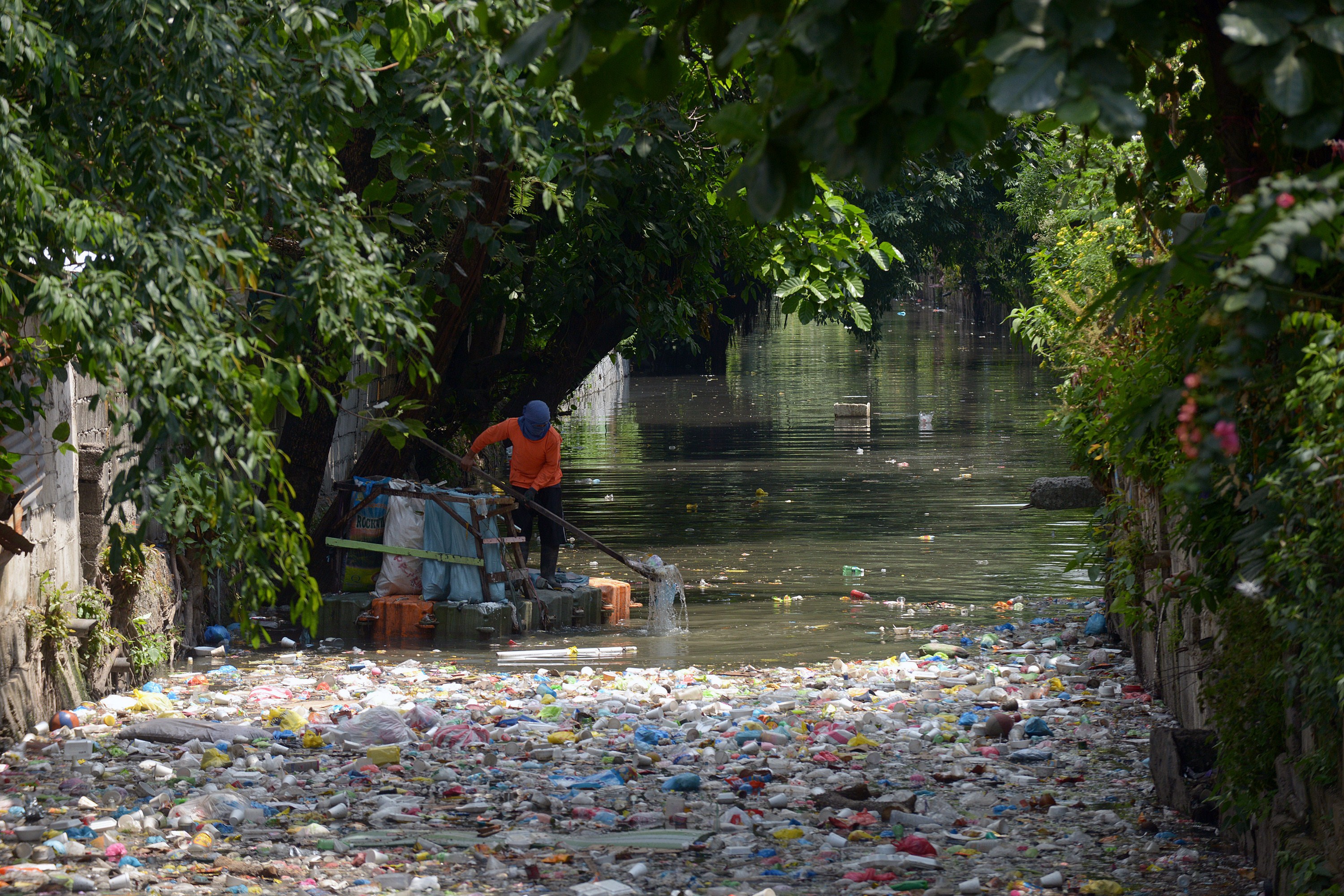 A clean-up volunteer scoops plastic waste at an open sewer in Manila on May 4, 2015. Non-governmental environmental groups are calling for national legislation to prevent plastic waste that clog waterways.