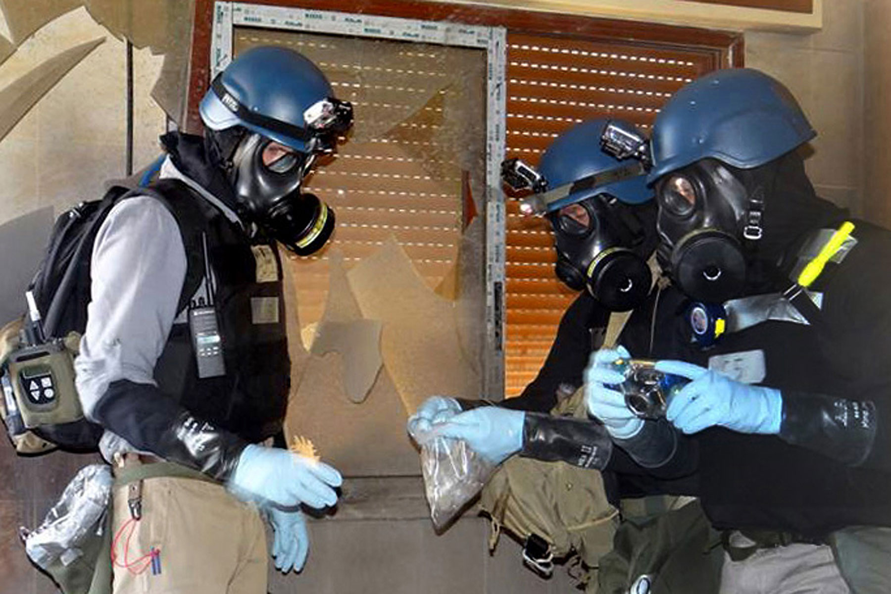 In this Thursday, Aug. 29, 2013 file citizen journalism image provided by the Local Committee of Arbeen which has been authenticated based on its contents and other AP reporting, members of the UN investigation team take samples from the ground in the Damascus countryside of Zamalka, Syria