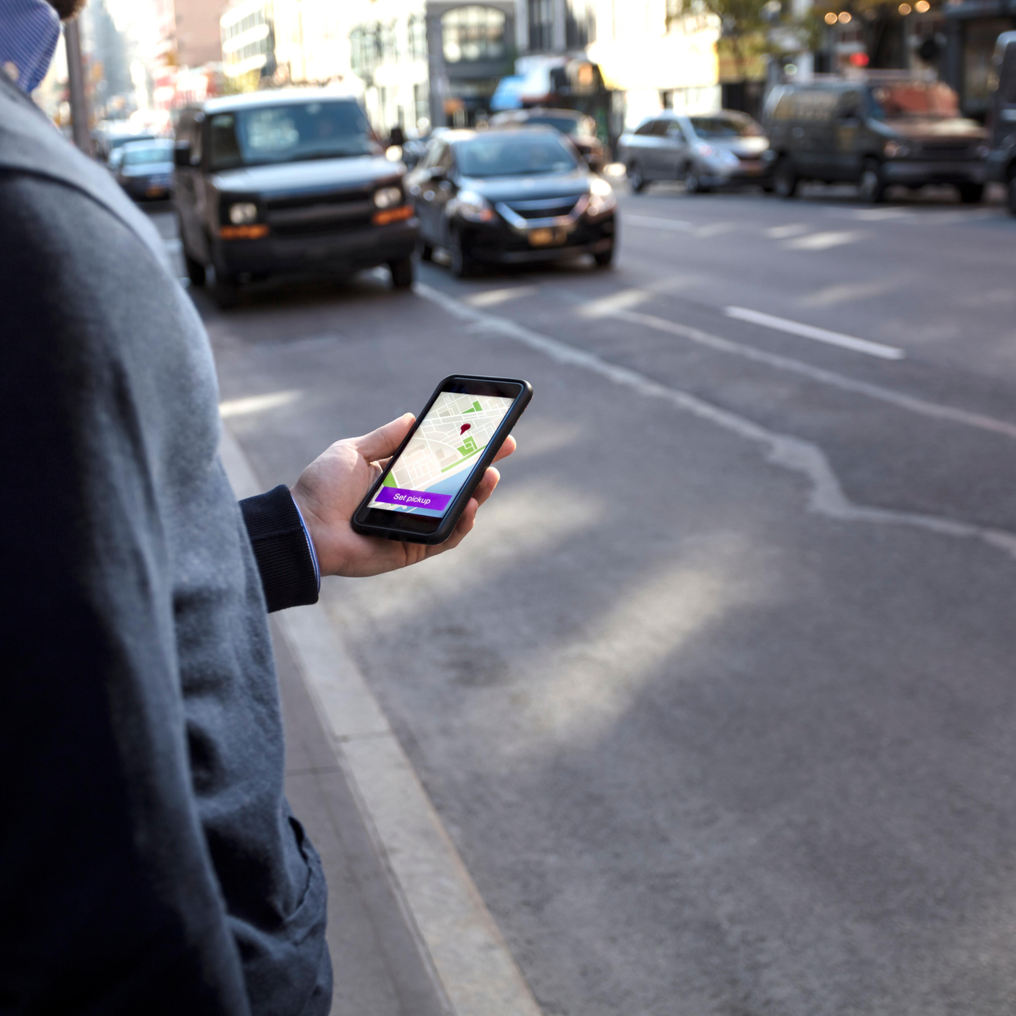 Young man holding cell phone waiting for car