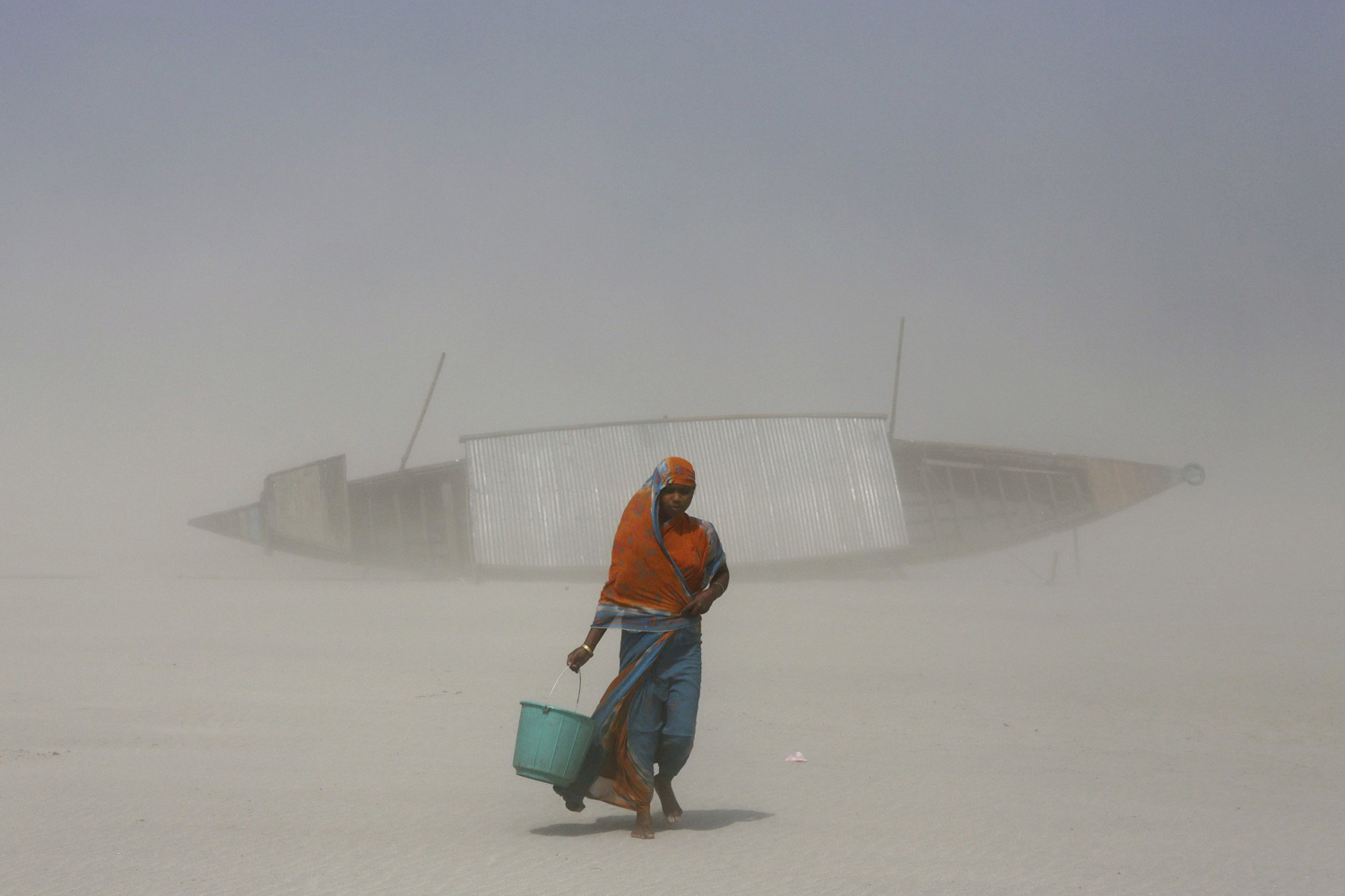 An Indian woman carries a bucket filled with drinking water as she walks on dry mud against blowing sand, along the Brahmaputra river on the eve of World Water Day in Gauhati, India, March 21, 2014.