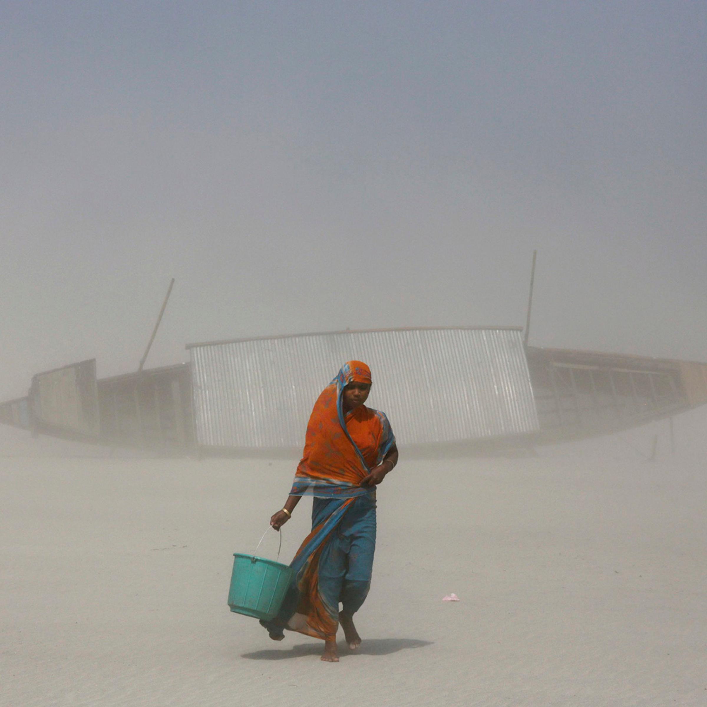 An Indian woman carries a bucket filled with drinking water as she walks on dry mud against blowing sand, along the Brahmaputra river on the eve of World Water Day in Gauhati, India, March 21, 2014.
