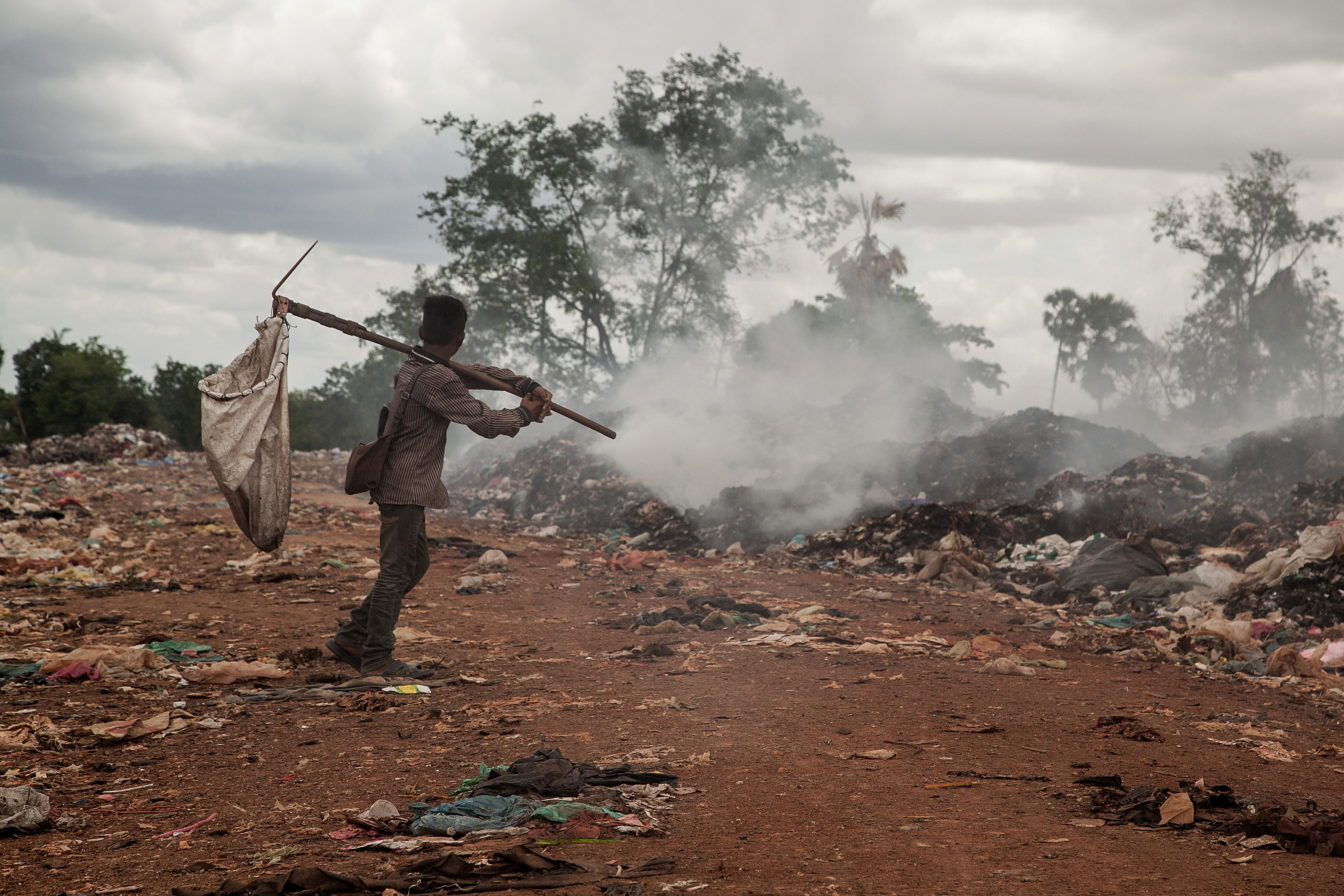 A young scavenger walks near a burning pile of trash in the Anlong Pi landfill on June 11, 2014 in Siem Reap, Cambodia.