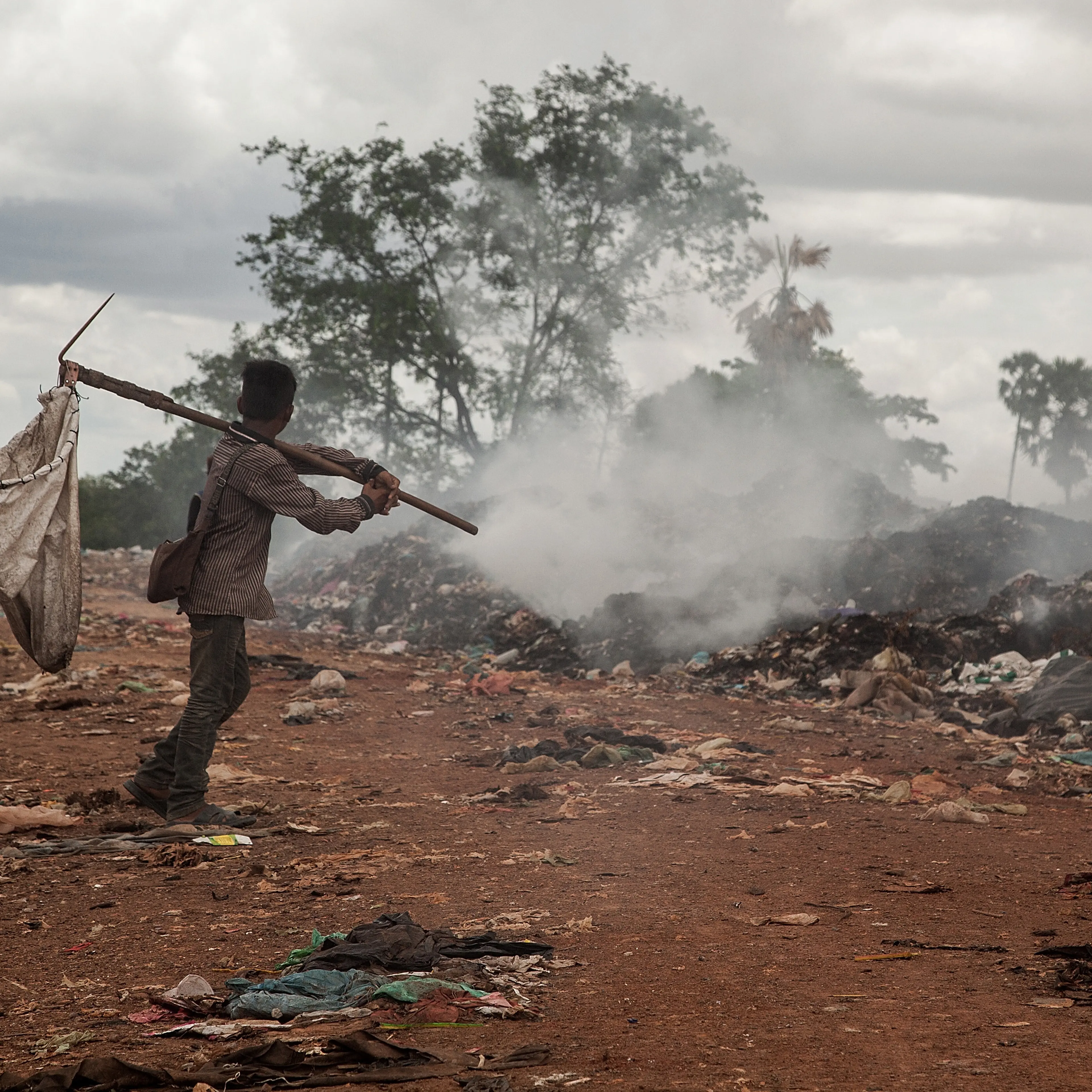 A young scavenger walks near a burning pile of trash in the Anlong Pi landfill on June 11, 2014 in Siem Reap, Cambodia.