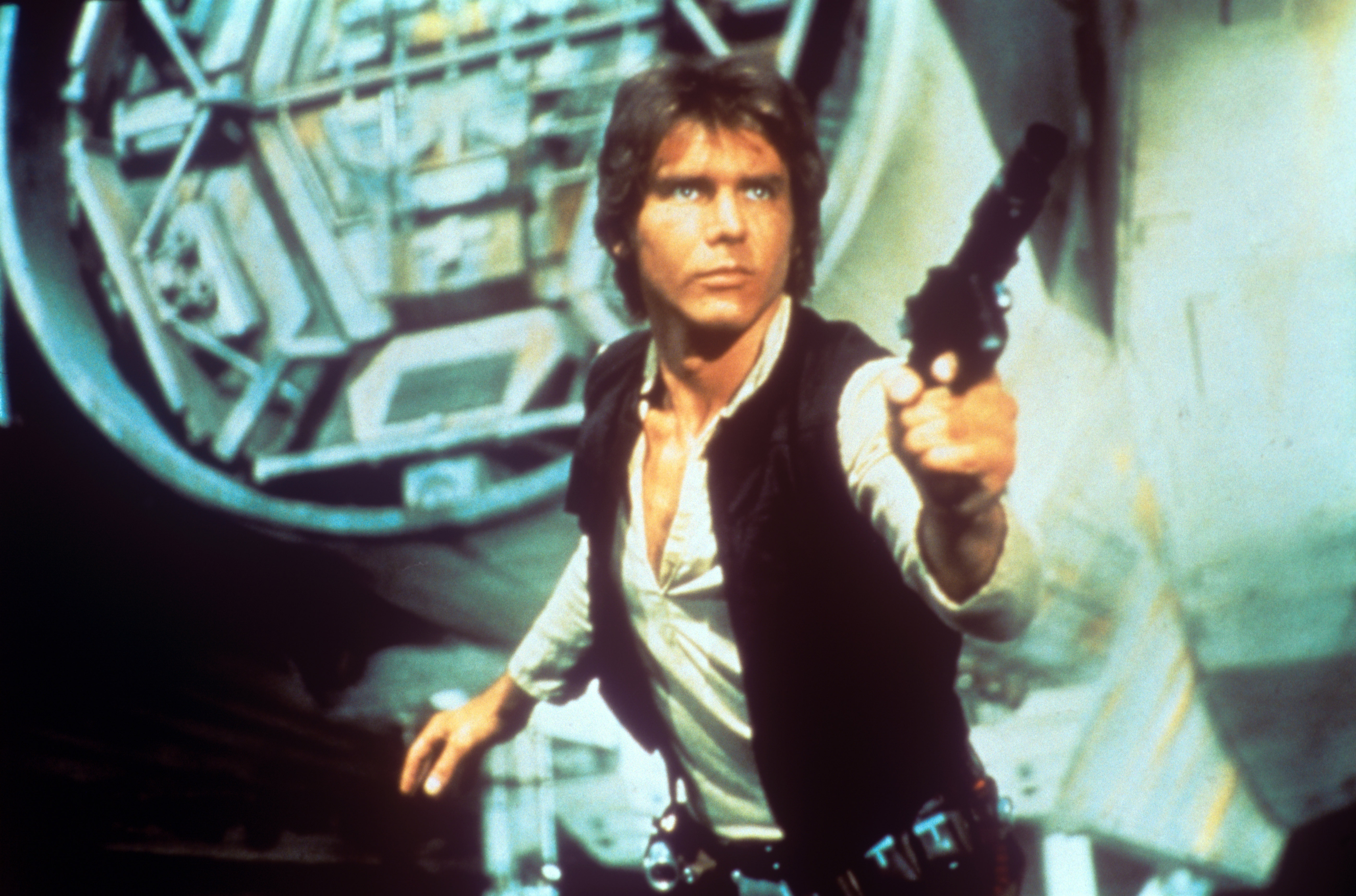In a scene from George Lucas' epic space opera Star Wars, the American actor Harrison Ford as rebel smuggler Han Solo draws a gun against enemies; behind him can be seen a fantastic space shuttle. USA, 1977.