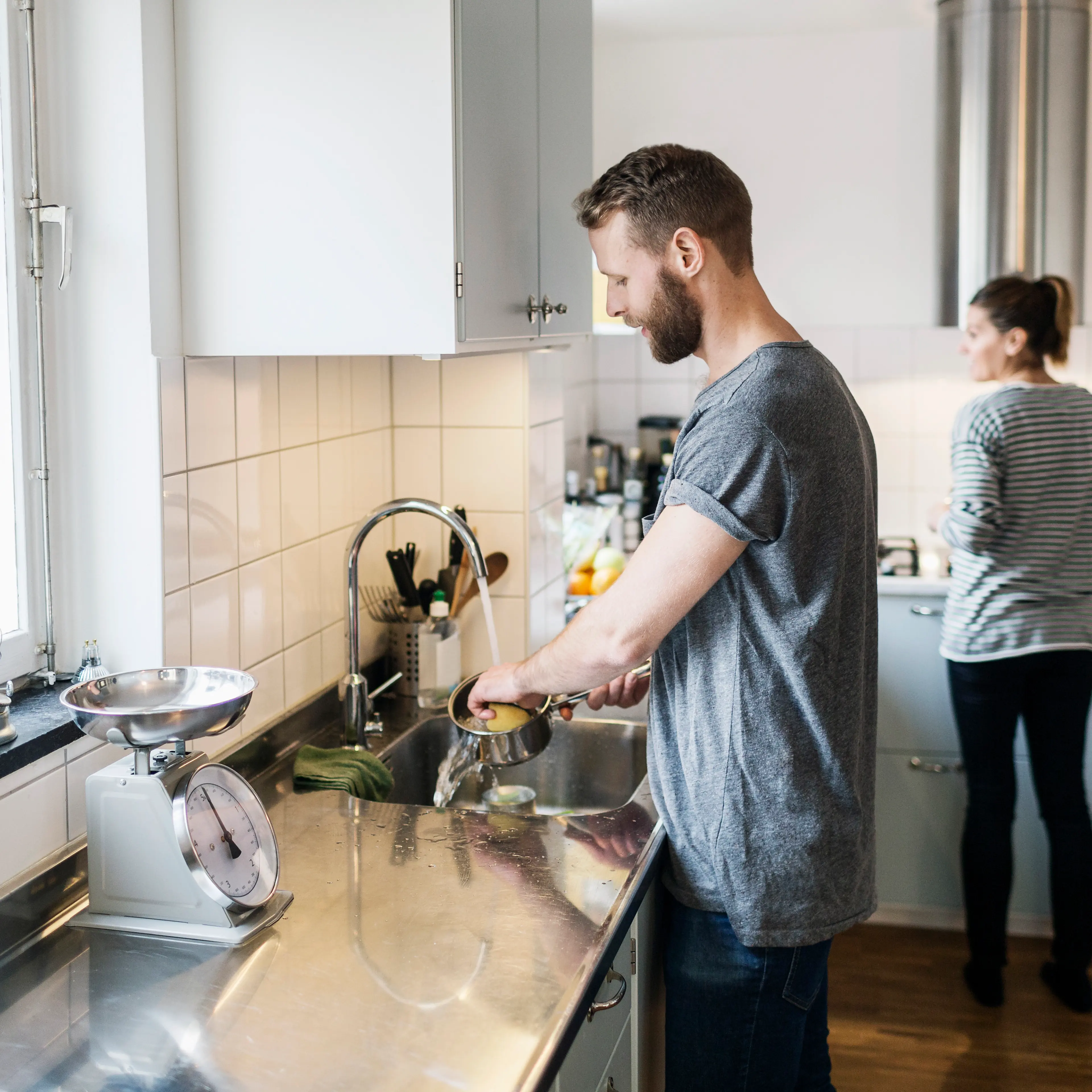 Man washing sauce pan while woman standing in background in kitchen