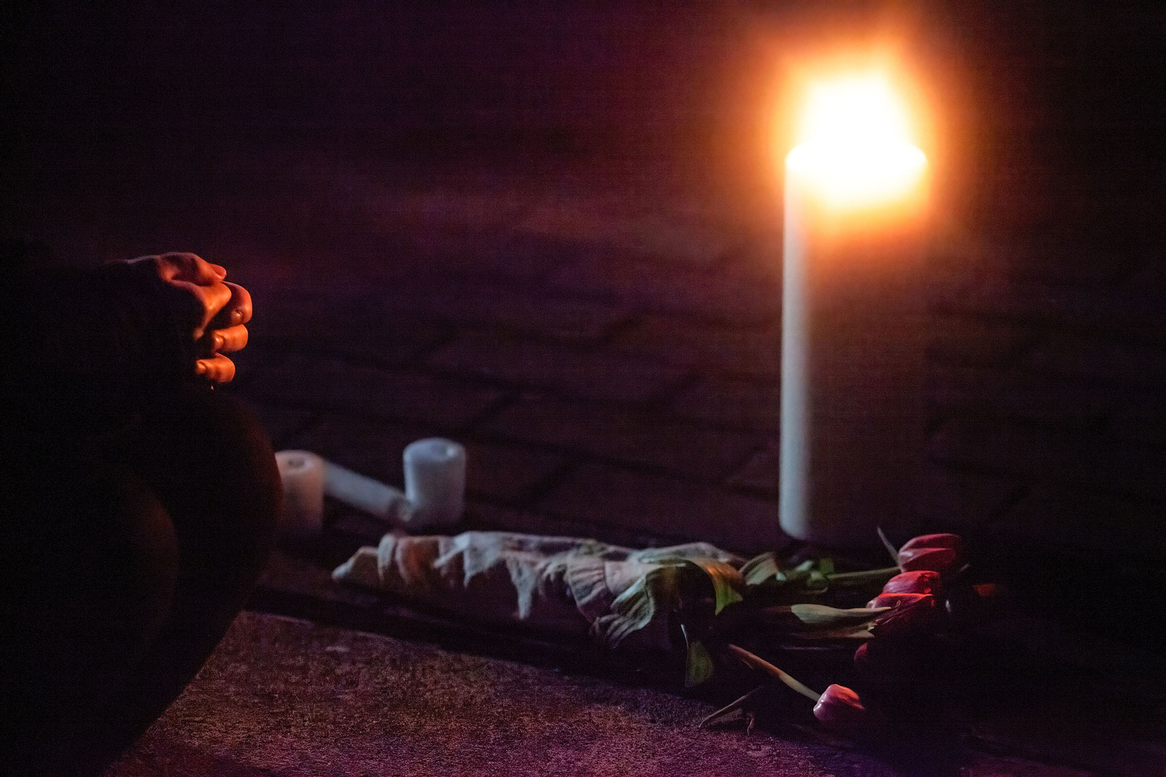 An attendee of a vigil kneels in front of a candle and flowers in memory of those who were killed in the shooting in Atlanta, on March 20, 2021.