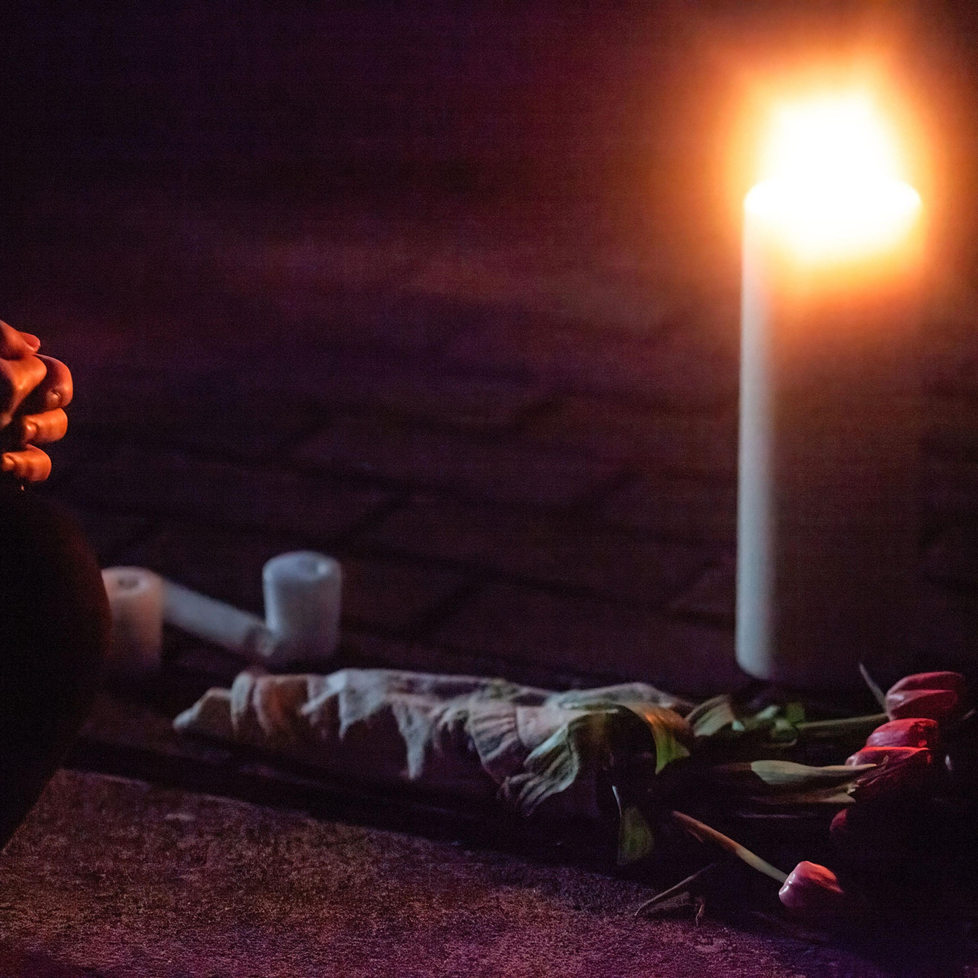 An attendee of a vigil kneels in front of a candle and flowers in memory of those who were killed in the shooting in Atlanta, on March 20, 2021.