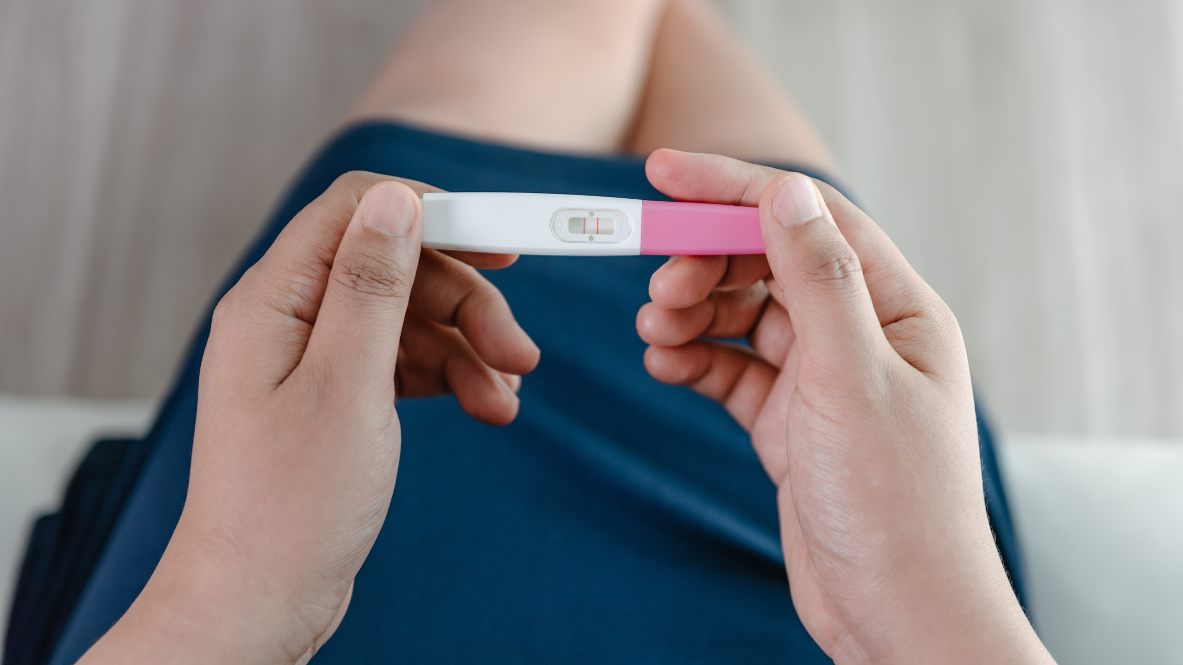 Close-Up of Young Woman Hands Holding a Pregnancy Test Kit and Waiting for Positive Result in Her Bedroom.