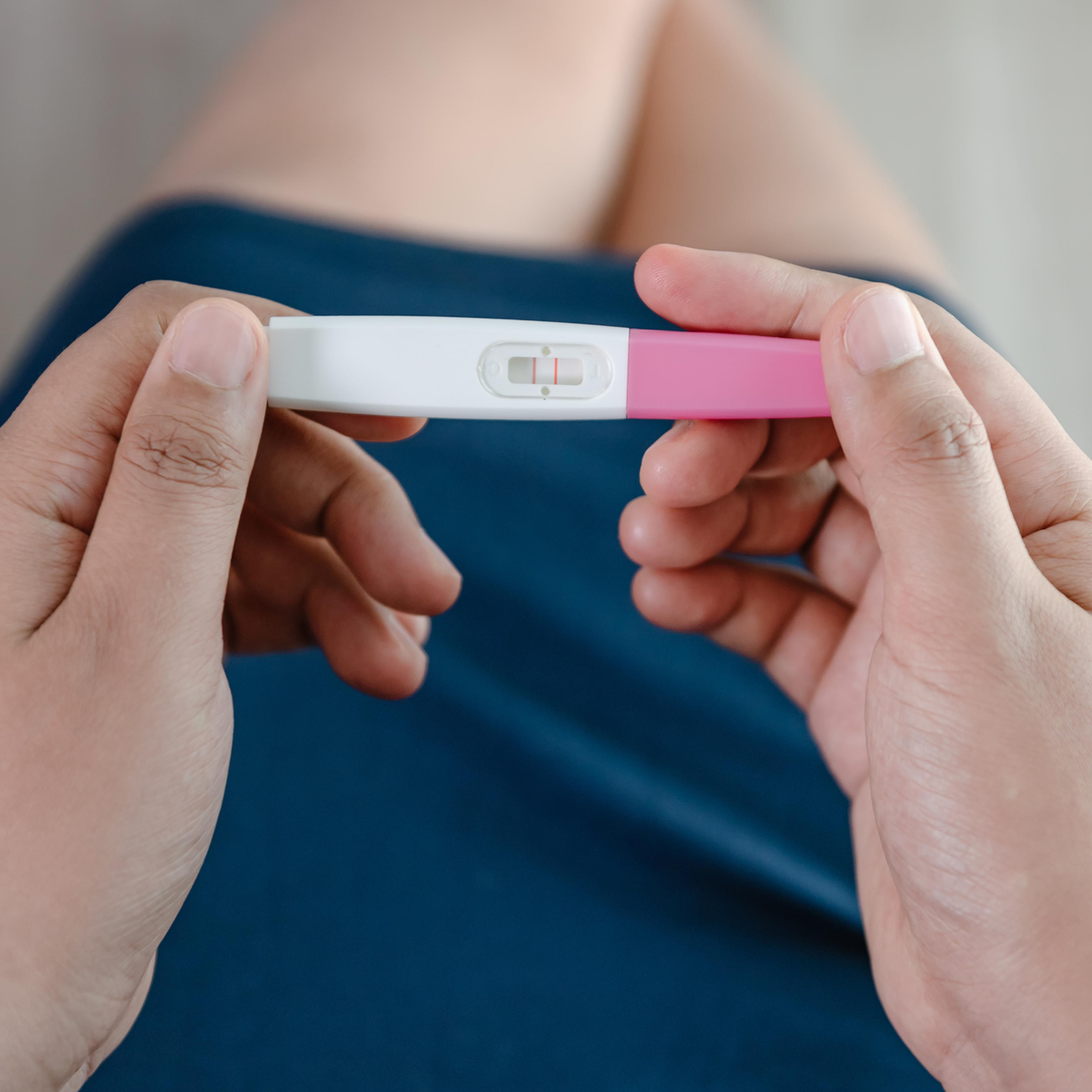 Close-Up of Young Woman Hands Holding a Pregnancy Test Kit and Waiting for Positive Result in Her Bedroom.