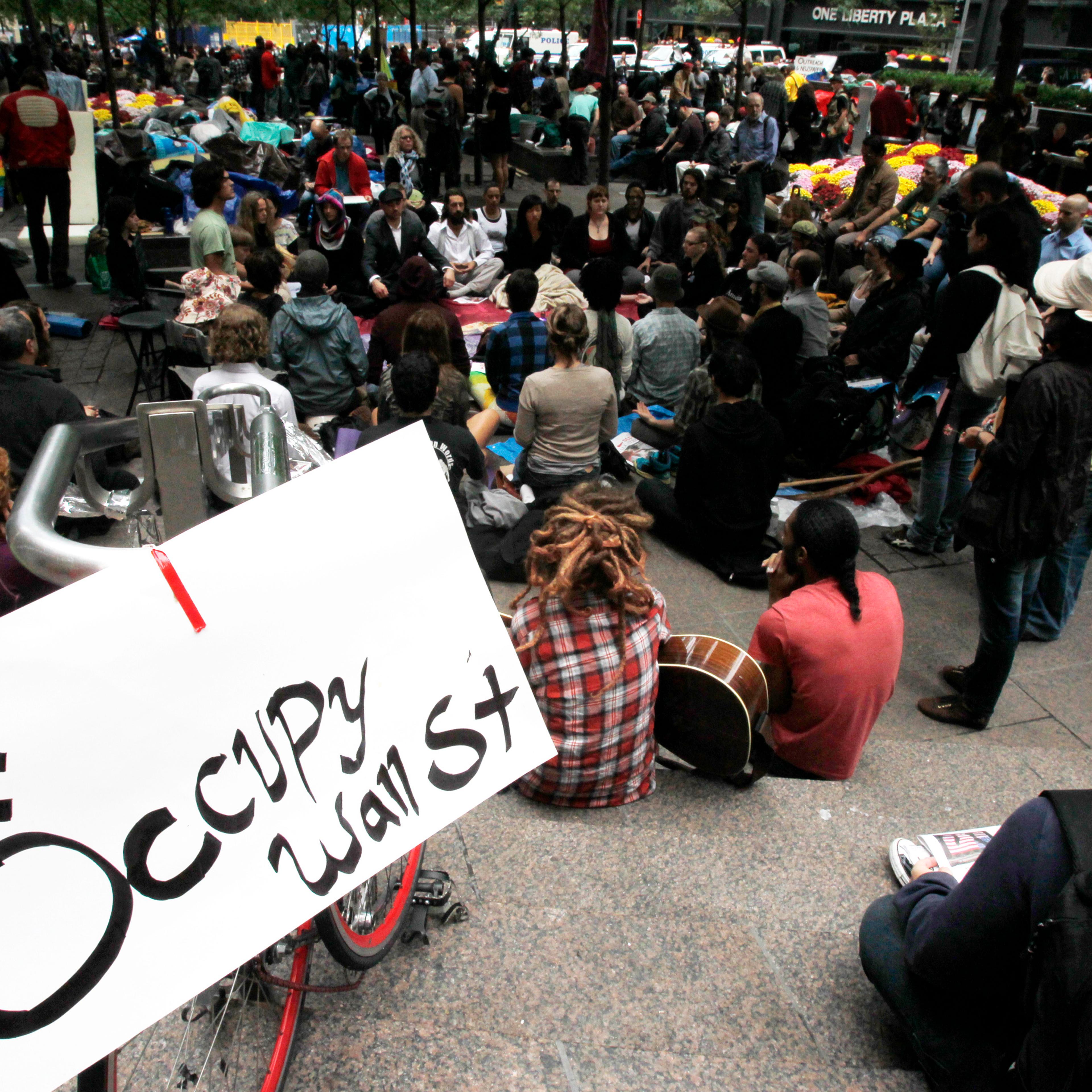 Occupy Wall Street protesters meditate while a sign bearing their twitter handle hangs from a railing in Zuccotti Park in New York