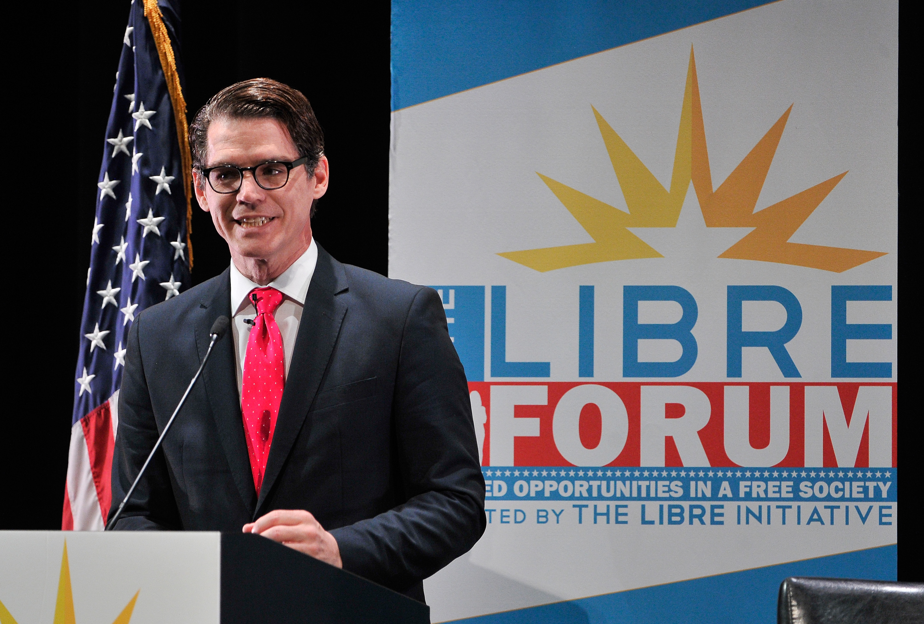 Daniel Garza addresses the crowd on stage in front of an American flag and the LIBRE Initiative poster