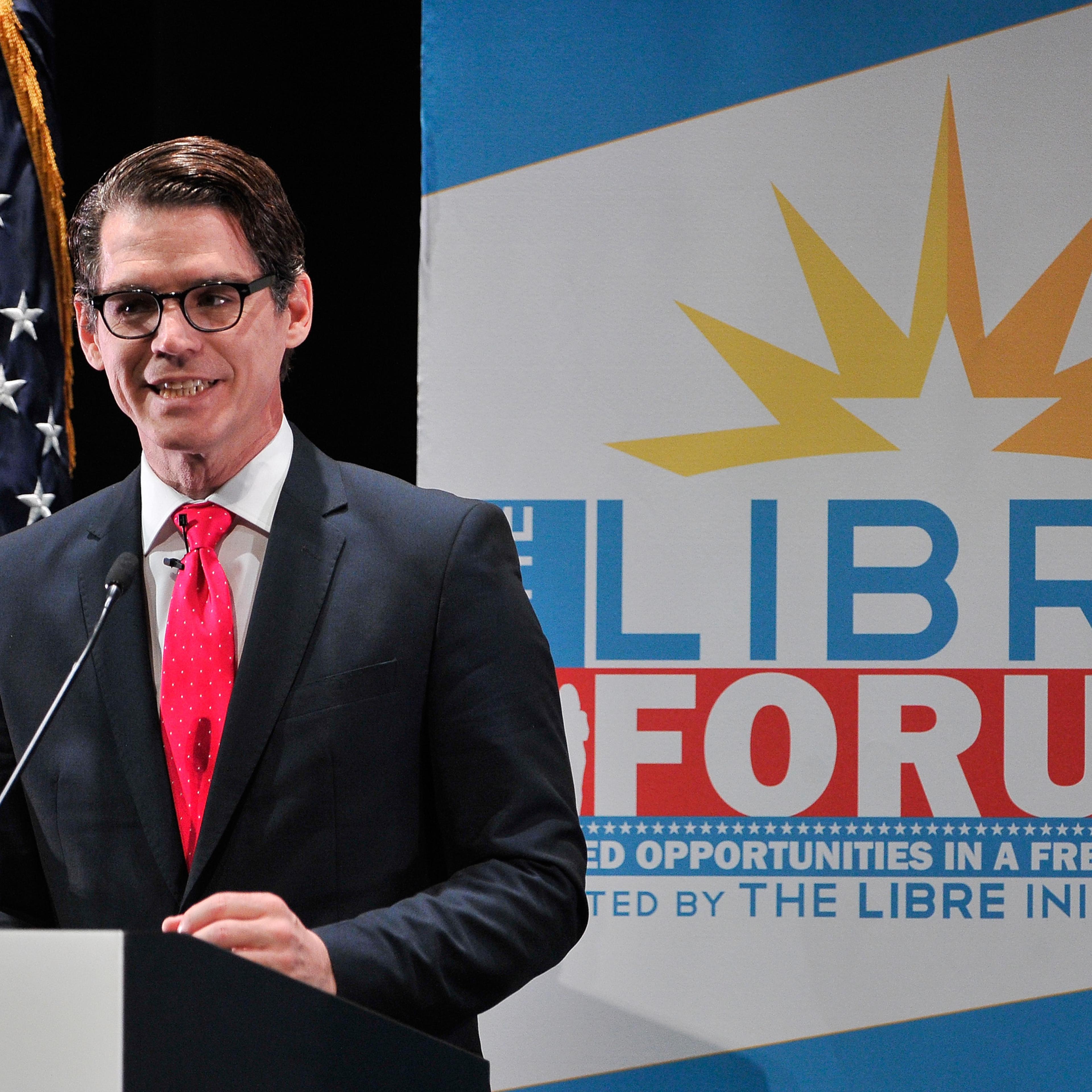 Daniel Garza addresses the crowd on stage in front of an American flag and the LIBRE Initiative poster