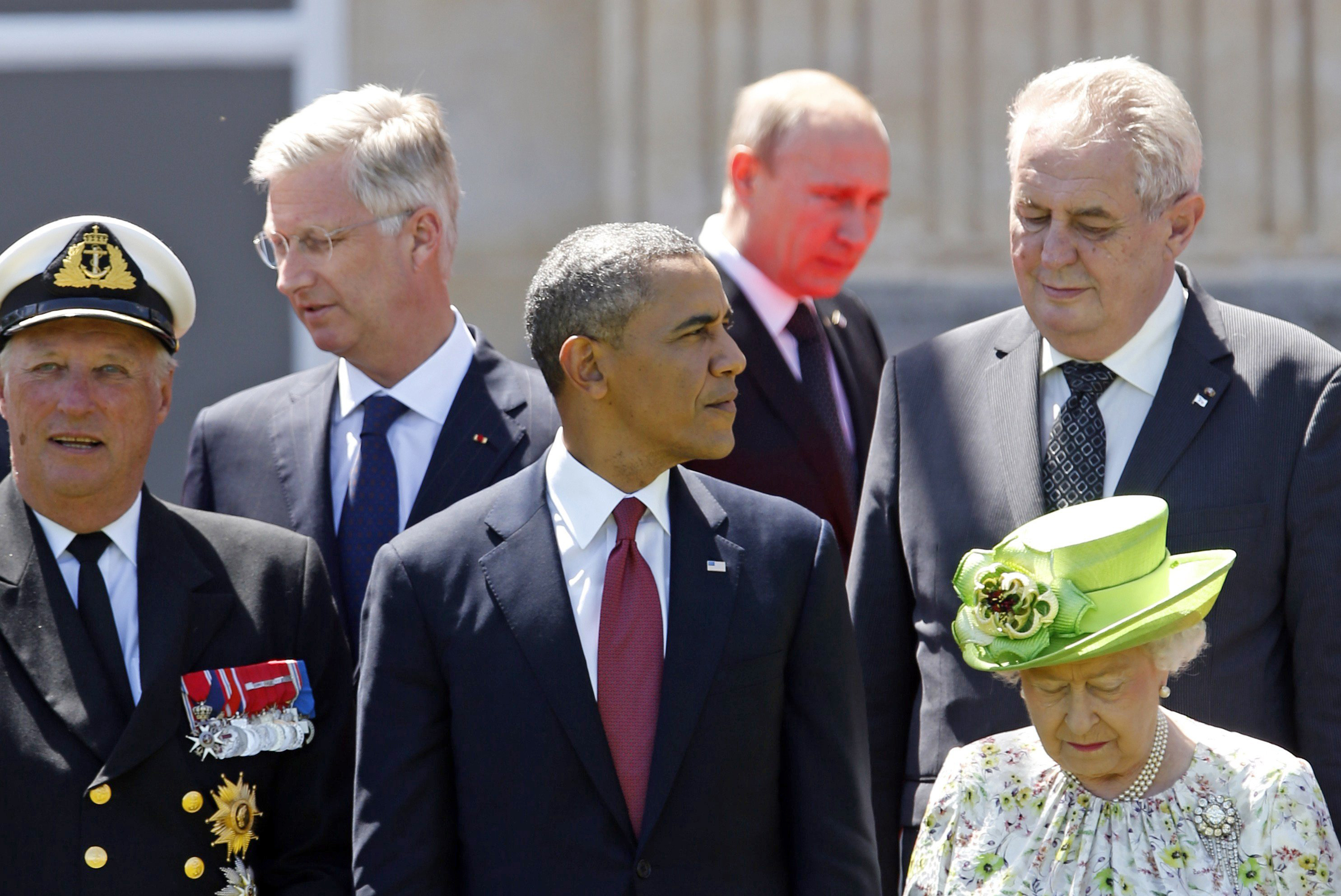 Red light reflected from the carpet illuminates Russian President Vladimir Putin as he passes U.S. President Barack Obama (center) and other leaders at a group photo for the 70th anniversary of the D-Day landings in Benouville June 6, 2014.
