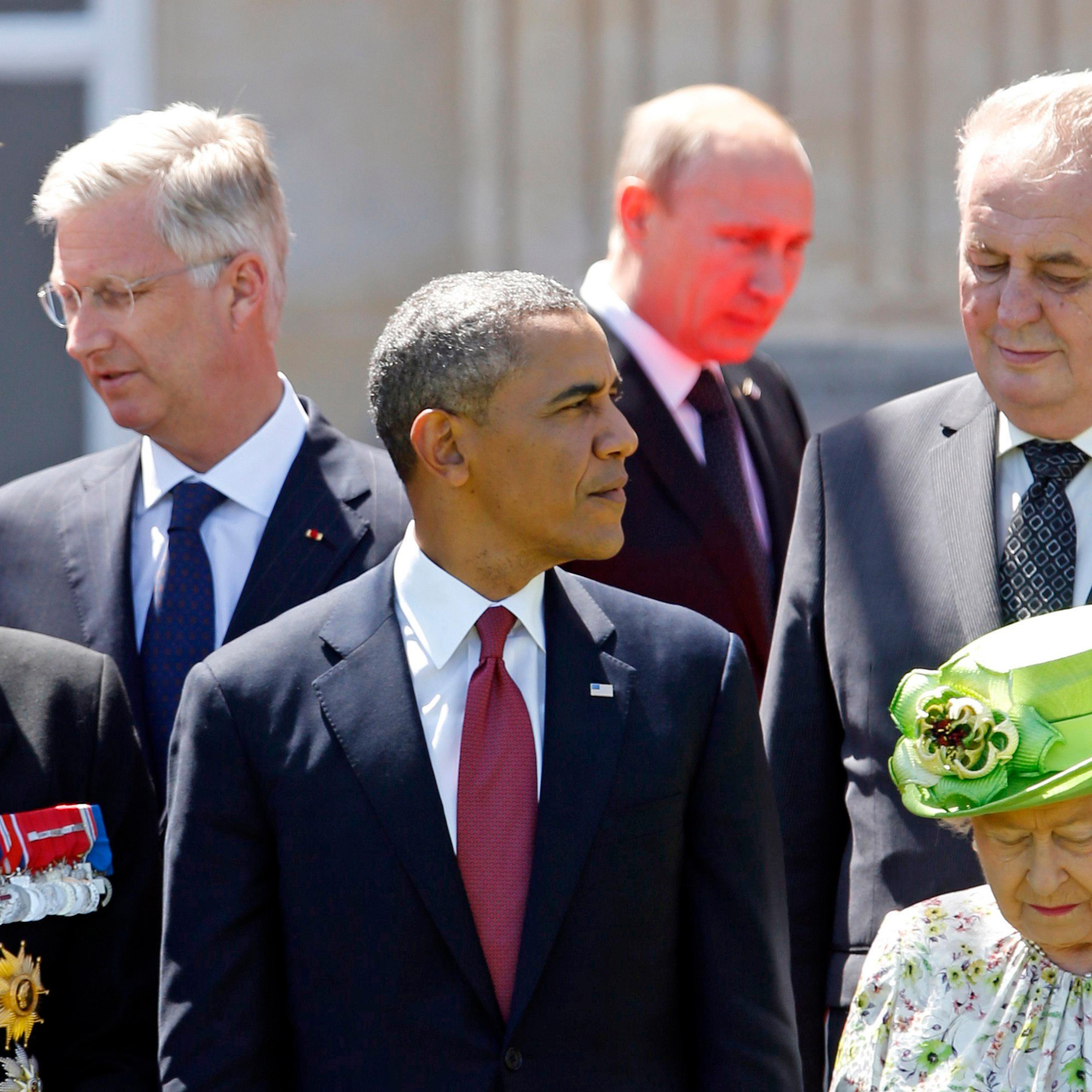 Red light reflected from the carpet illuminates Russian President Vladimir Putin as he passes U.S. President Barack Obama (center) and other leaders at a group photo for the 70th anniversary of the D-Day landings in Benouville June 6, 2014.