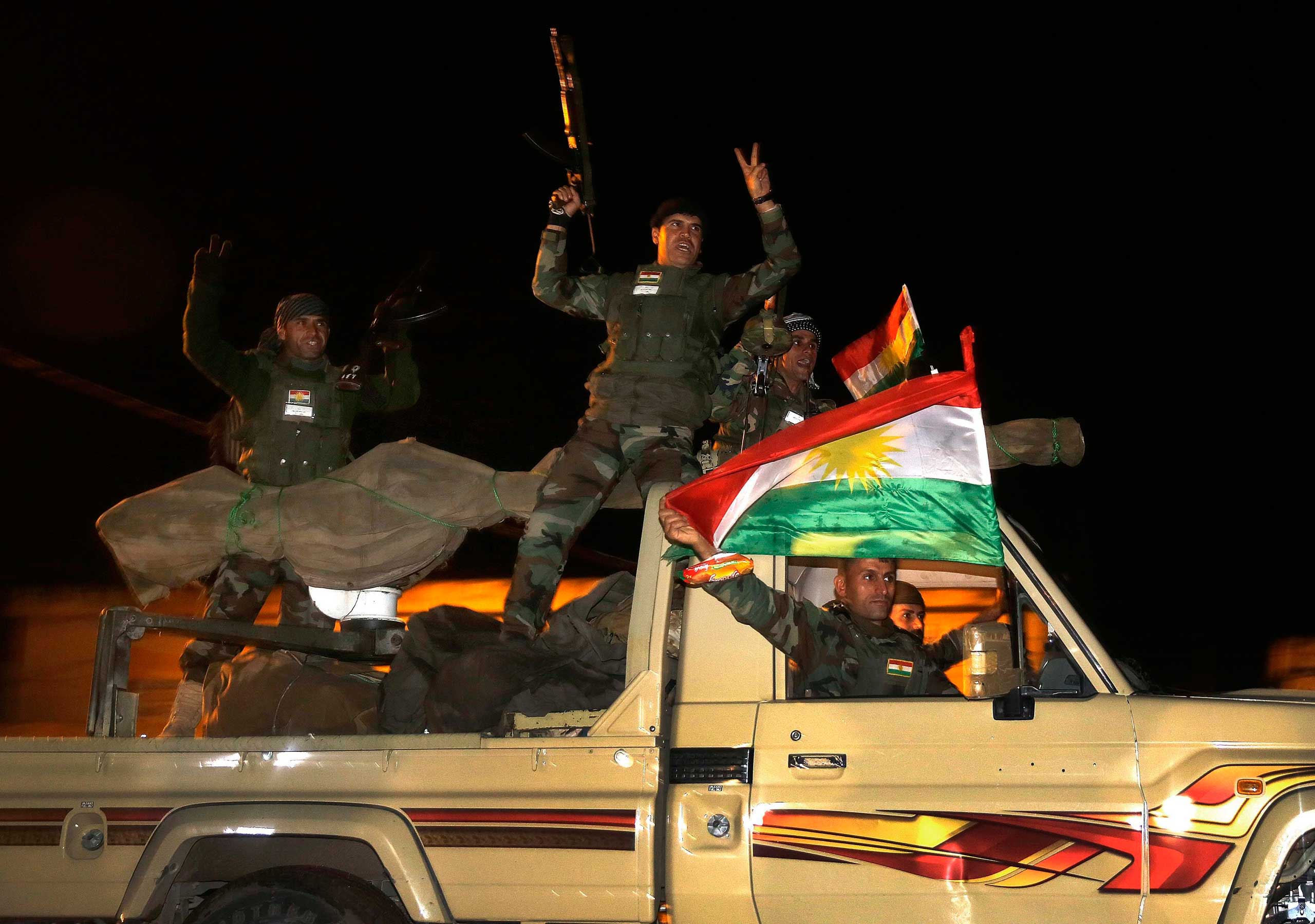 Kurdish peshmerga fighters wave flags as they move towards Kobani  from the Turkish town of Suruc