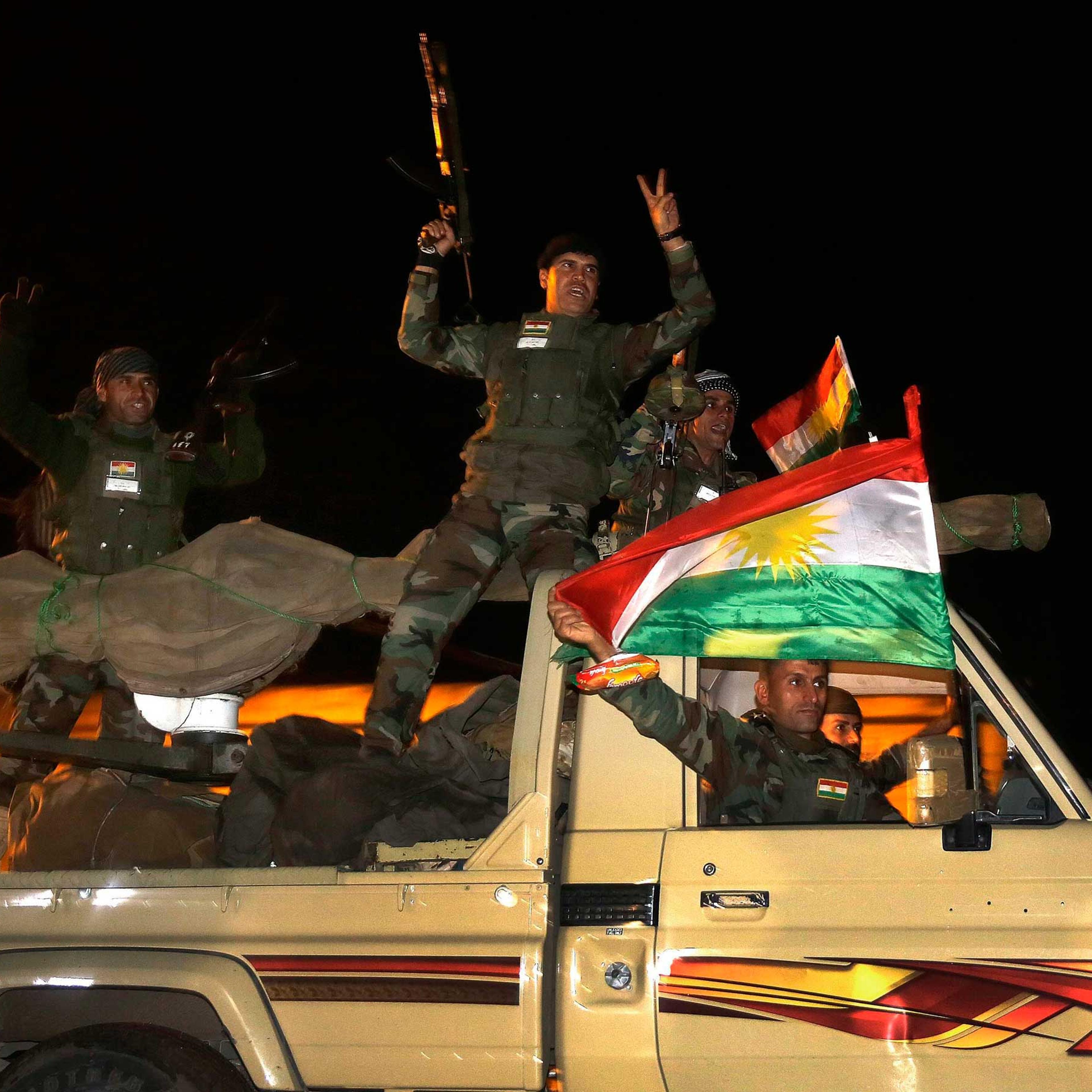 Kurdish peshmerga fighters wave flags as they move towards Kobani from the Turkish town of Suruc