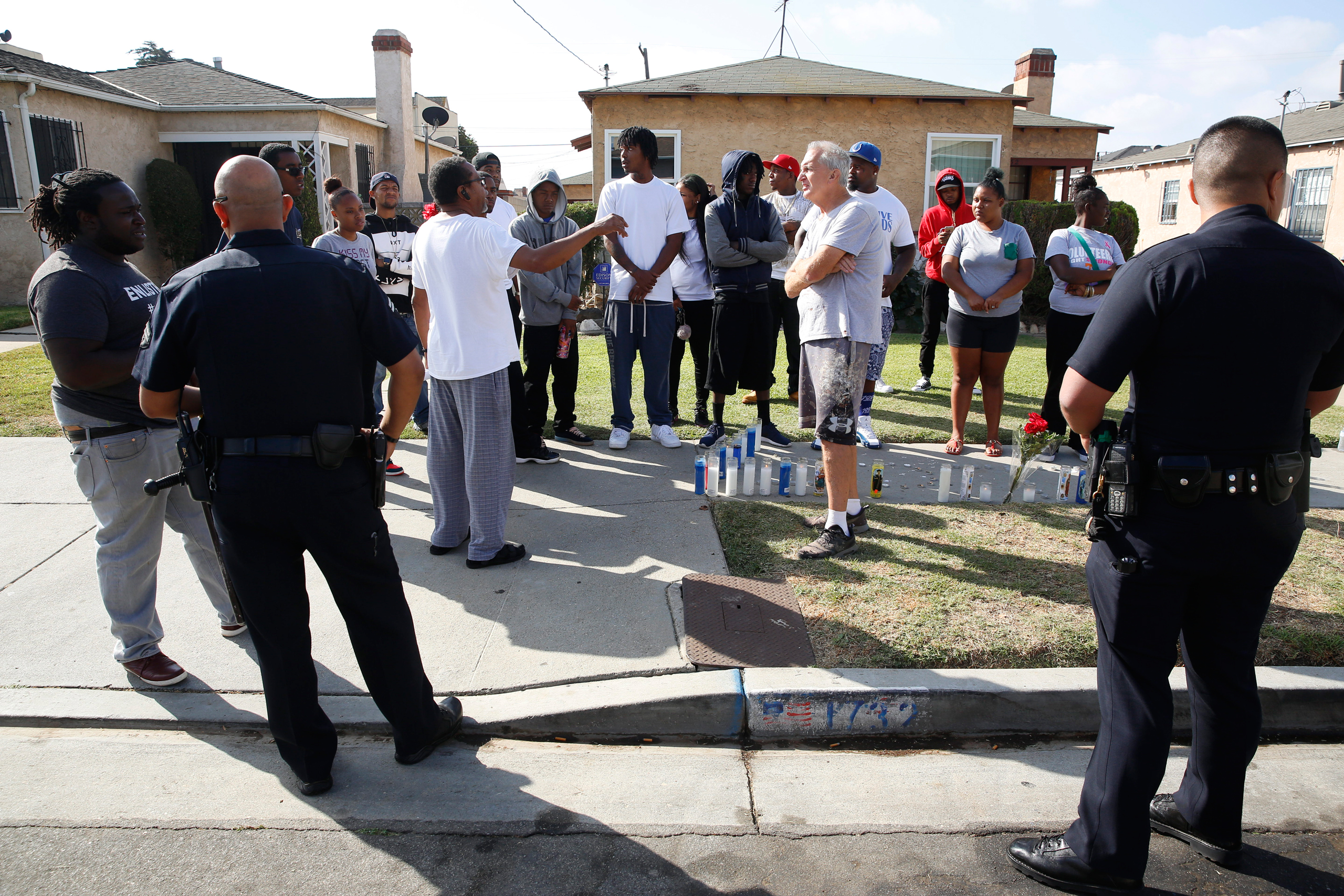 Los Angeles Police officers speak to neighbors and members of the community gathered around a makeshift memorial outside a residence on Sunday, Oct. 2, 2016. Officers shot and killed Carnell Snell Jr. in south Los Angeles on Saturday at the end of a car 