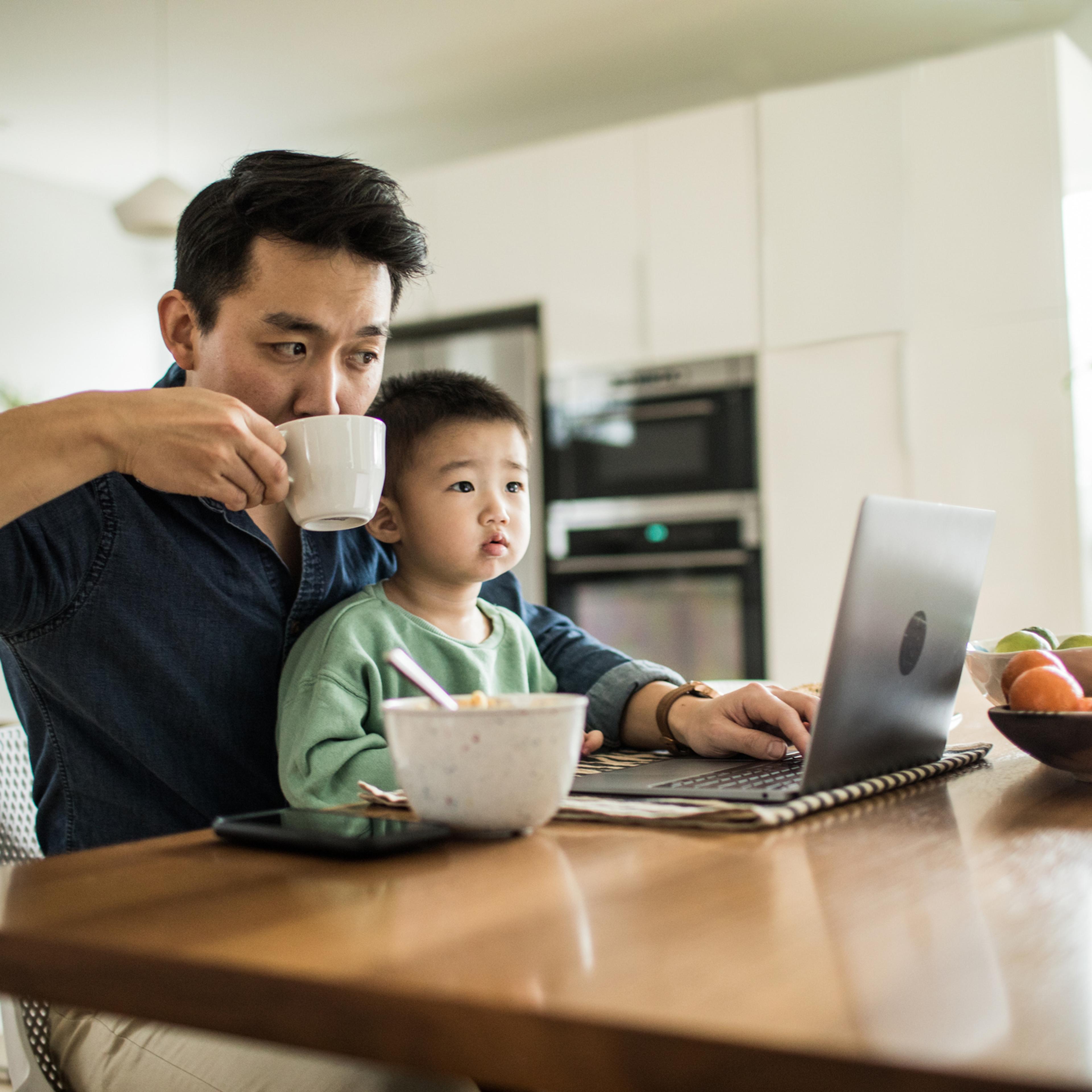Father multi-tasking with young son (2 yrs) at kitchen table