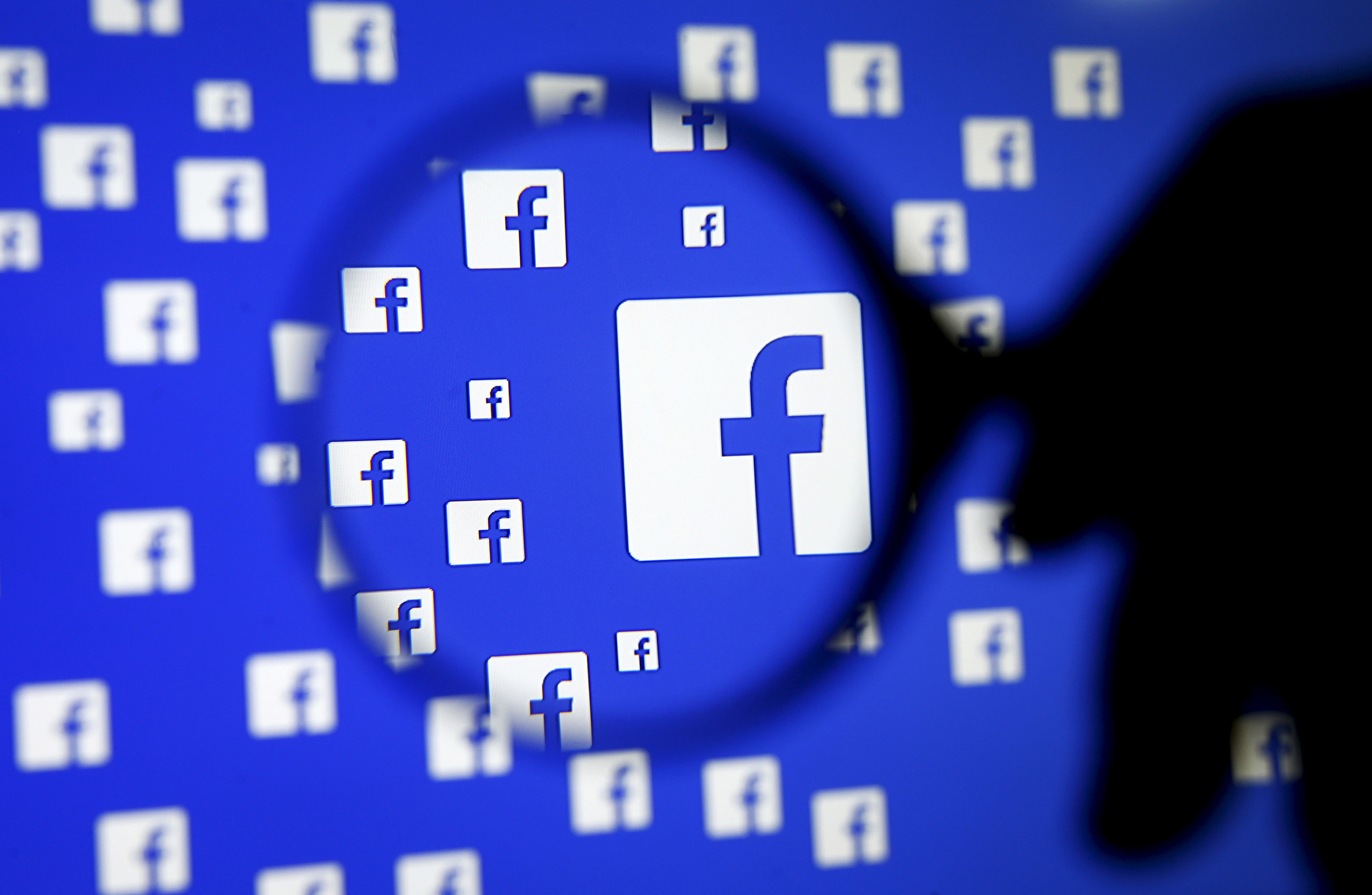 A man poses with a magnifier in front of a Facebook logo on display in this illustration taken in Sarajevo, Bosnia and Herzegovina, December 16, 2015. Facebook Inc said on Wednesday it is testing a service that will allow users of its Messenger app to ha