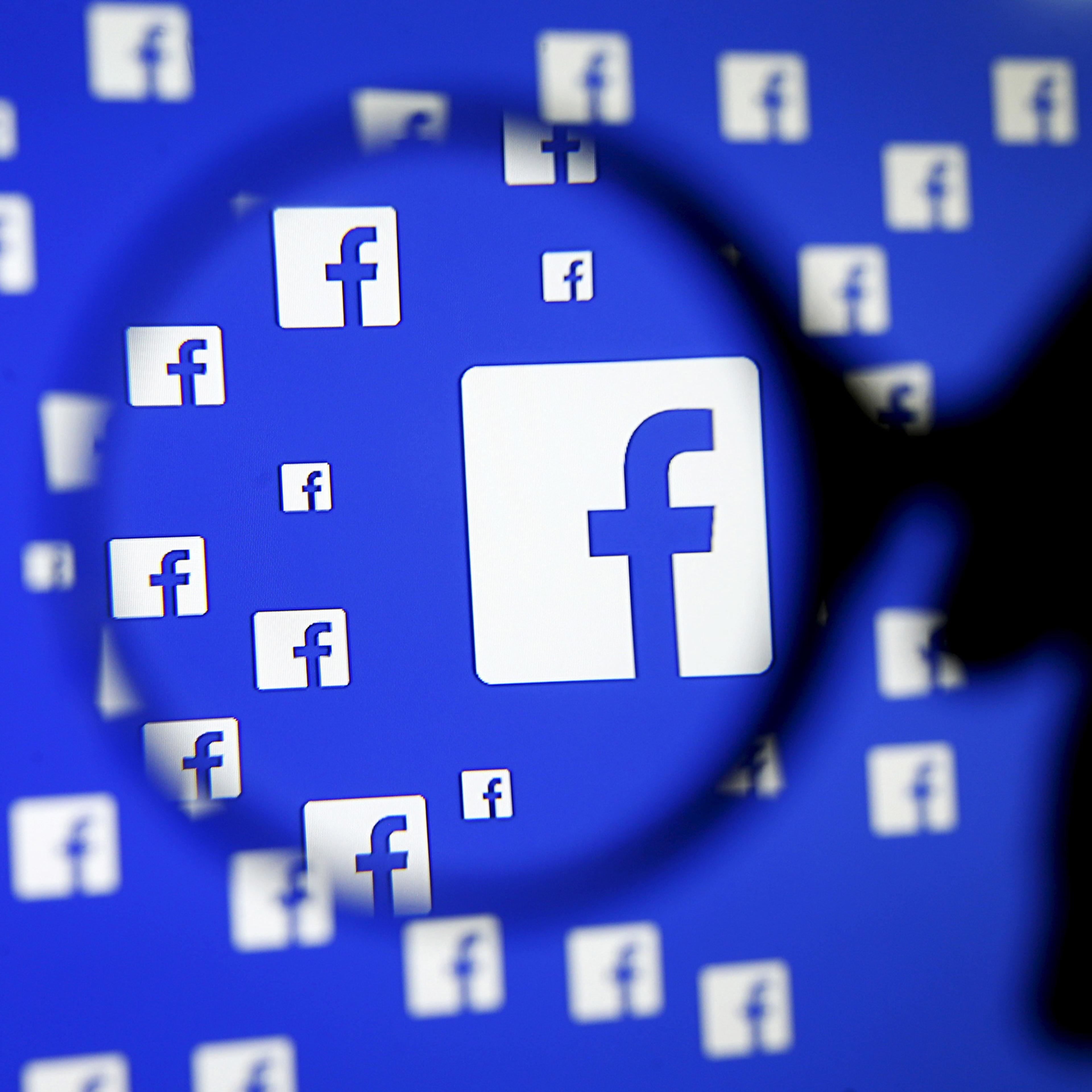 A man poses with a magnifier in front of a Facebook logo on display in this illustration taken in Sarajevo, Bosnia and Herzegovina, December 16, 2015. Facebook Inc said on Wednesday it is testing a service that will allow users of its Messenger app to ha