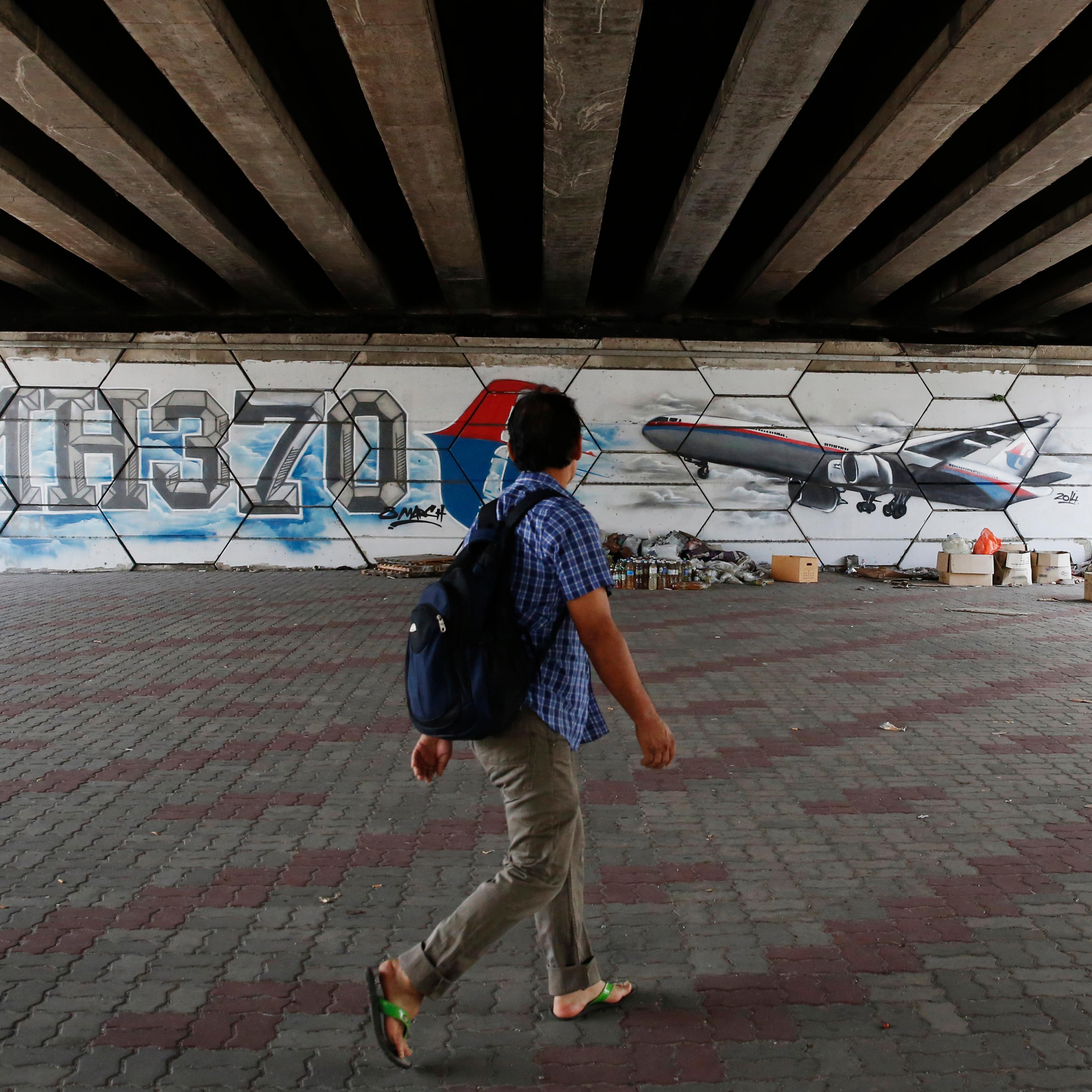 A man walks past graffiti depicting flight MH370 on the one year anniversary of its disappearance in Kuala Lumpur