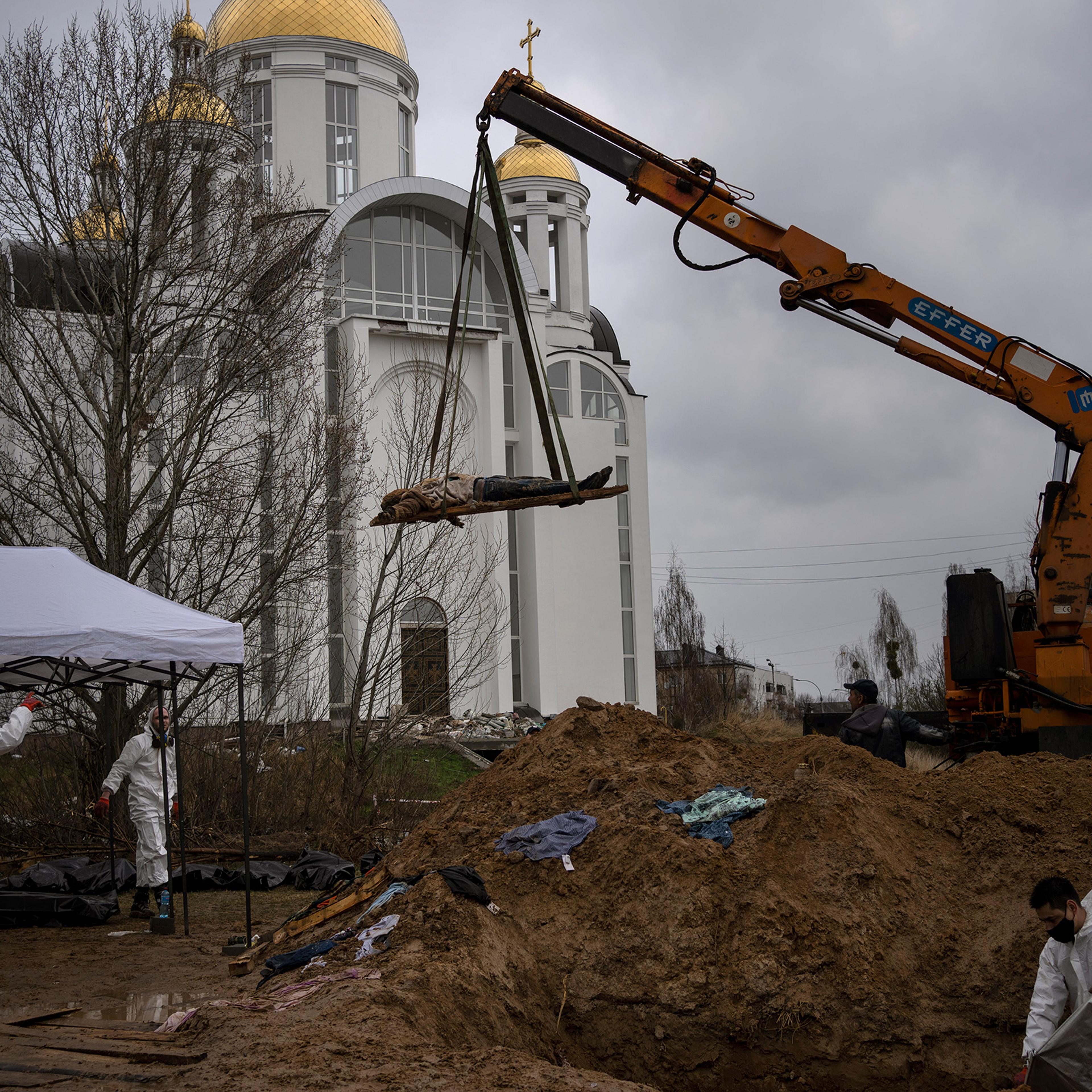 A crane lifts a corpse from a mass grave in Bucha; authorities say more than 400 civilians were murdered
