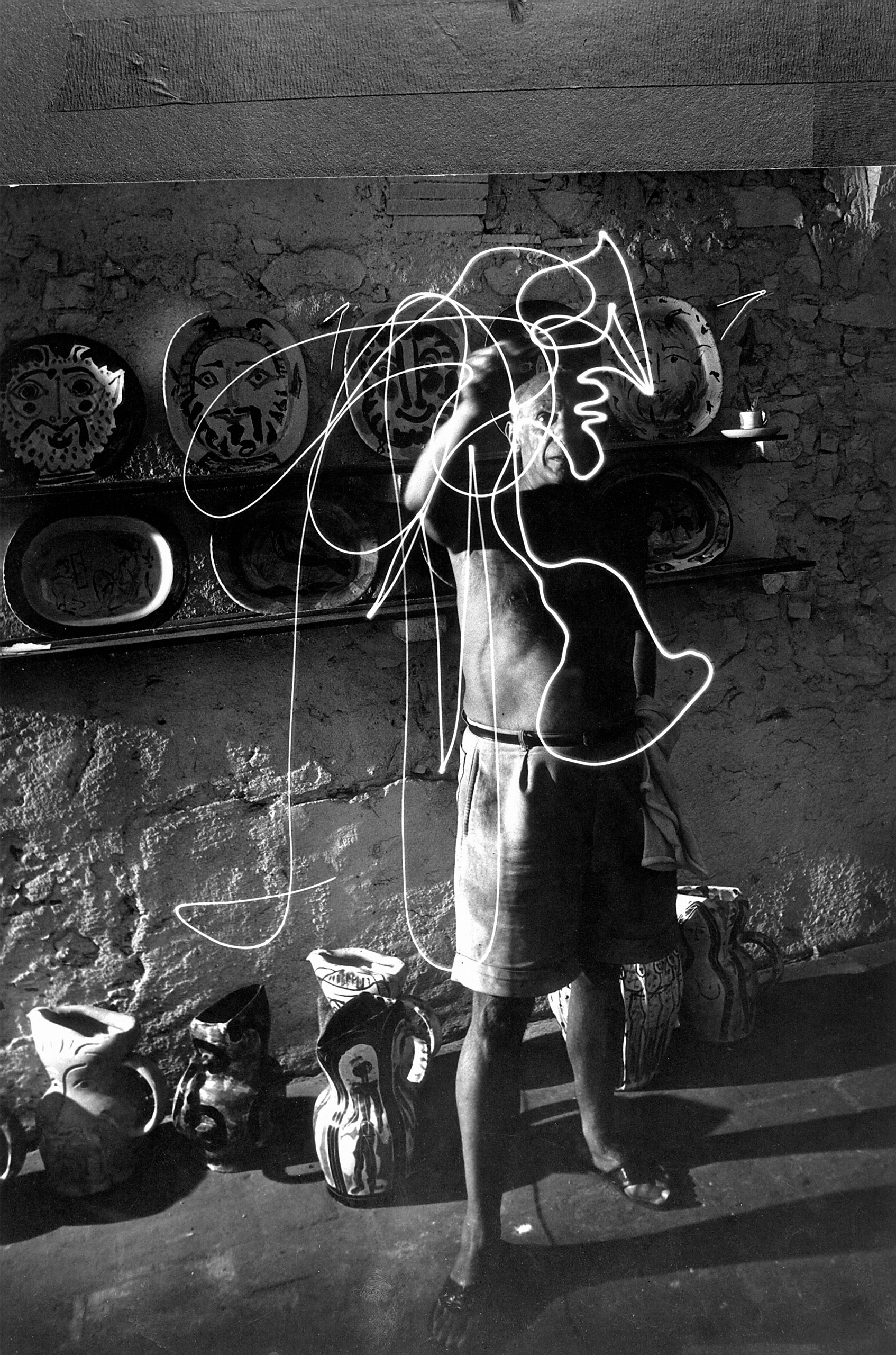 Pablo Picasso in his studio, "drawing" a profile with a pen light, 1949.