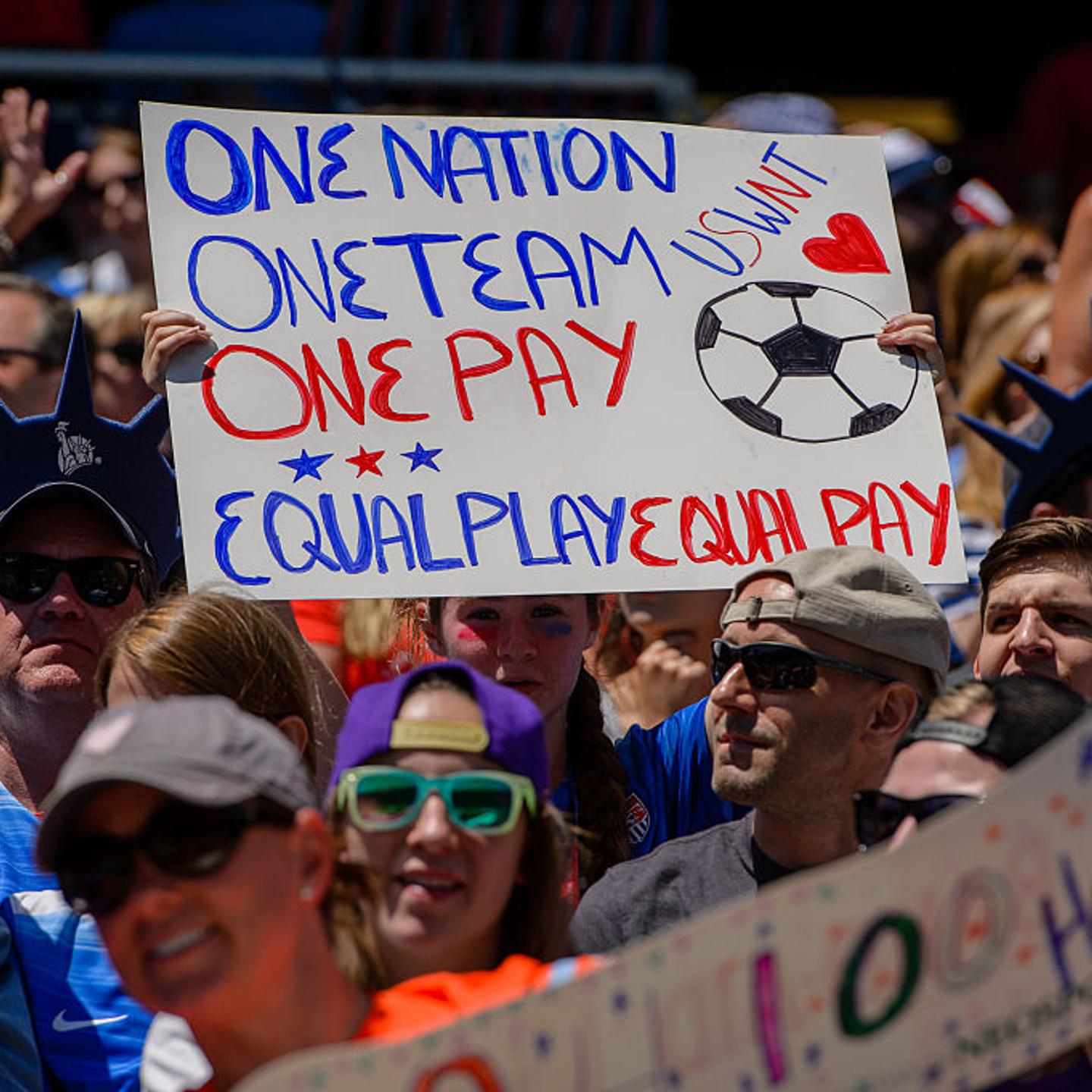 A fan holds an equal pay sign at a USWNT game
