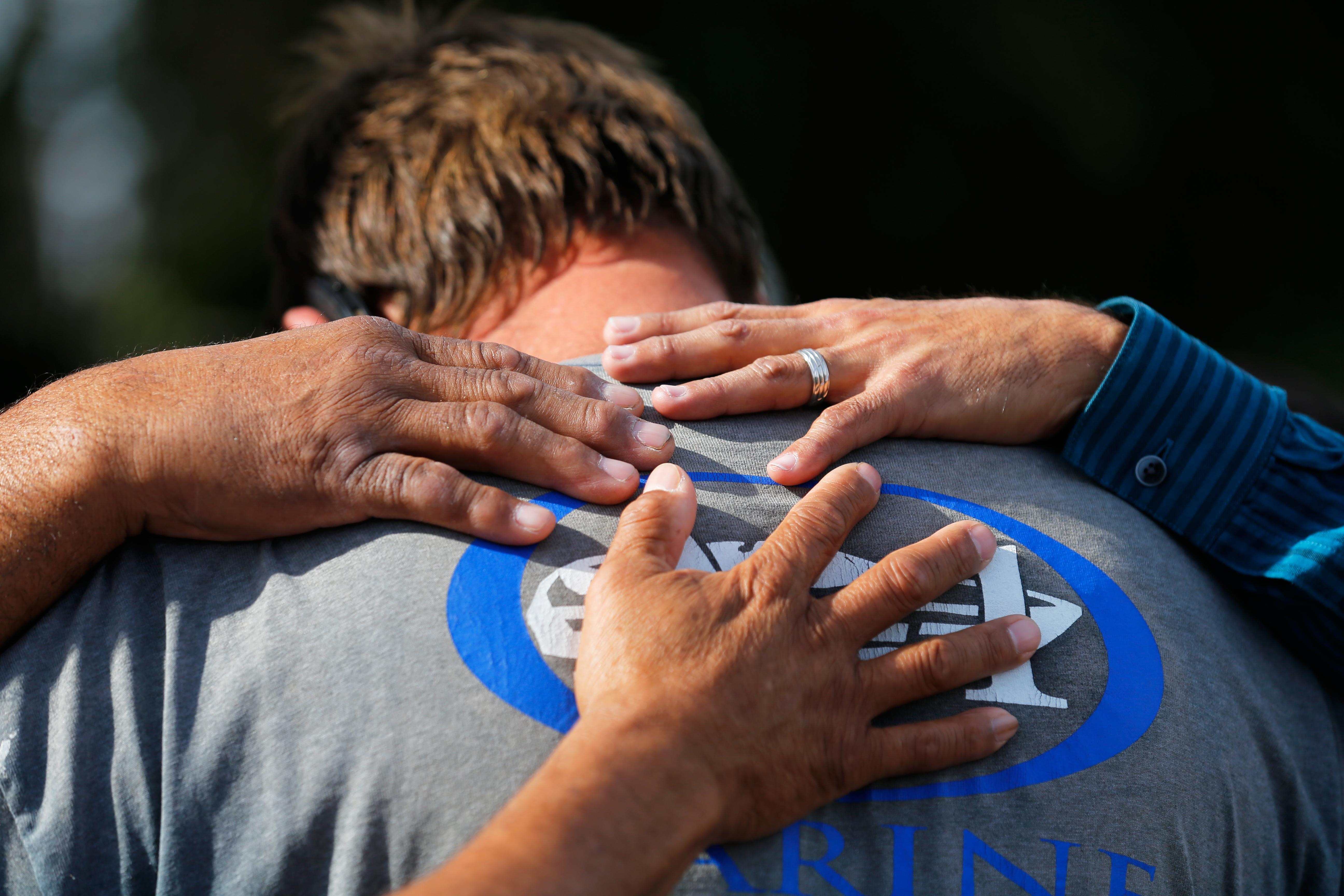 Neighbours comfort a man who was prevented from returning to his home at the scene of the investigation around the area of the SUV vehicle where two suspects were shot by police following a mass shooting in San Bernardino