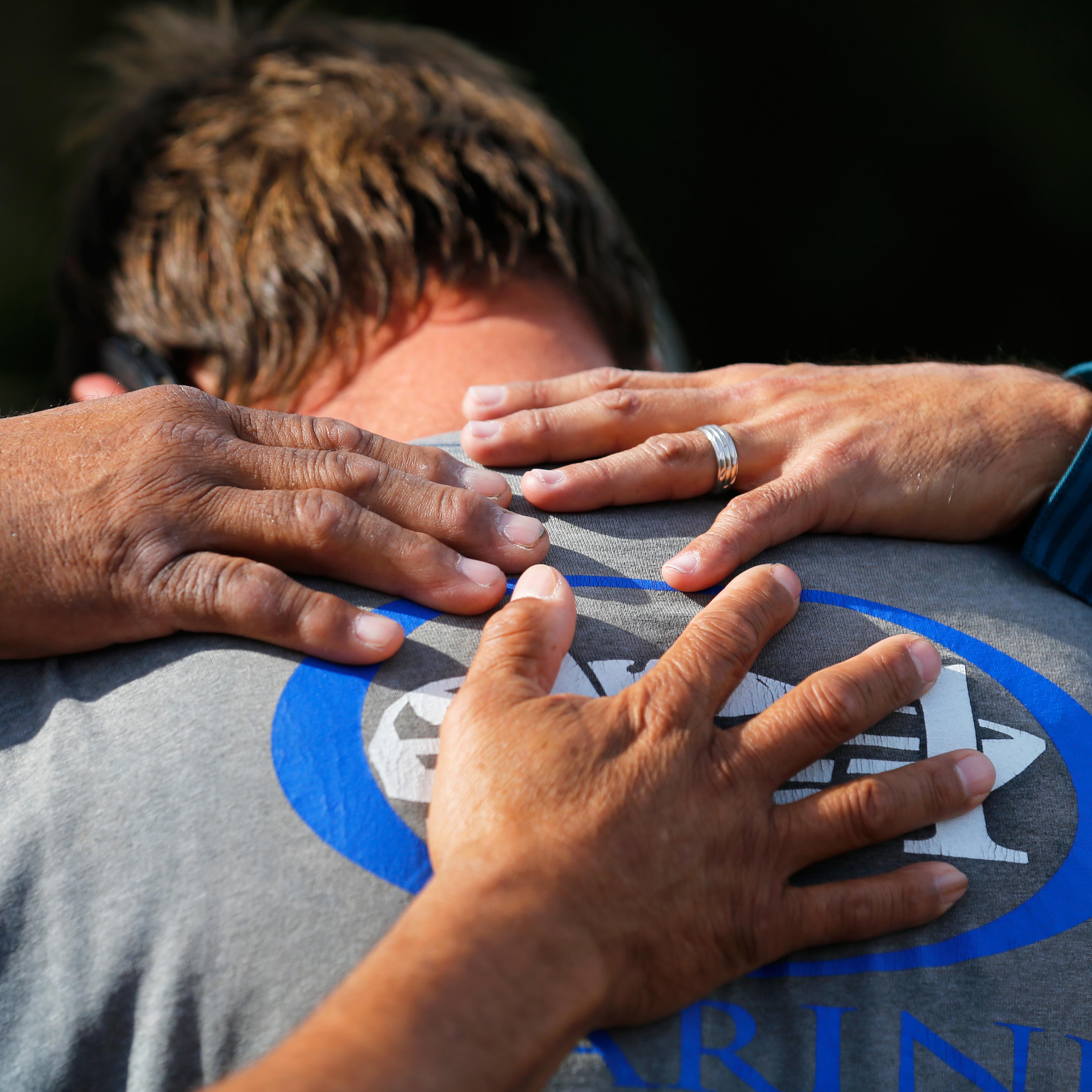 Neighbours comfort a man who was prevented from returning to his home at the scene of the investigation around the area of the SUV vehicle where two suspects were shot by police following a mass shooting in San Bernardino