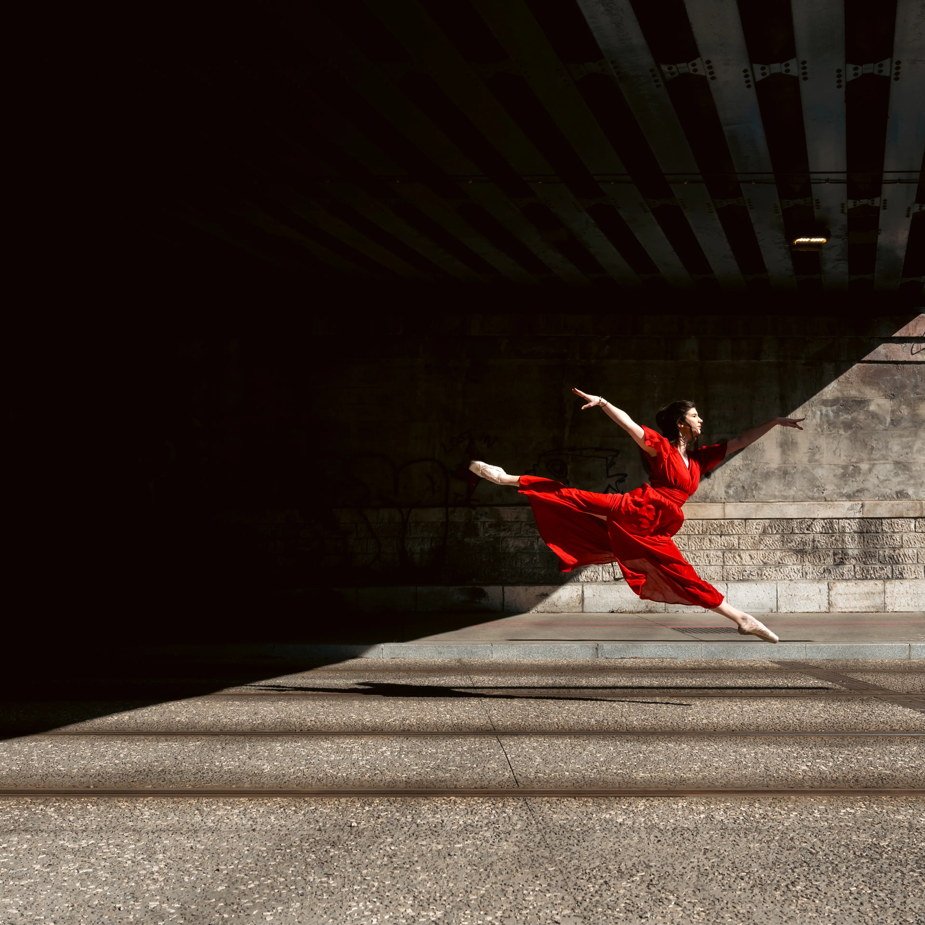 A ballet dancer in pointe shoes dances in the street with a long red dress.