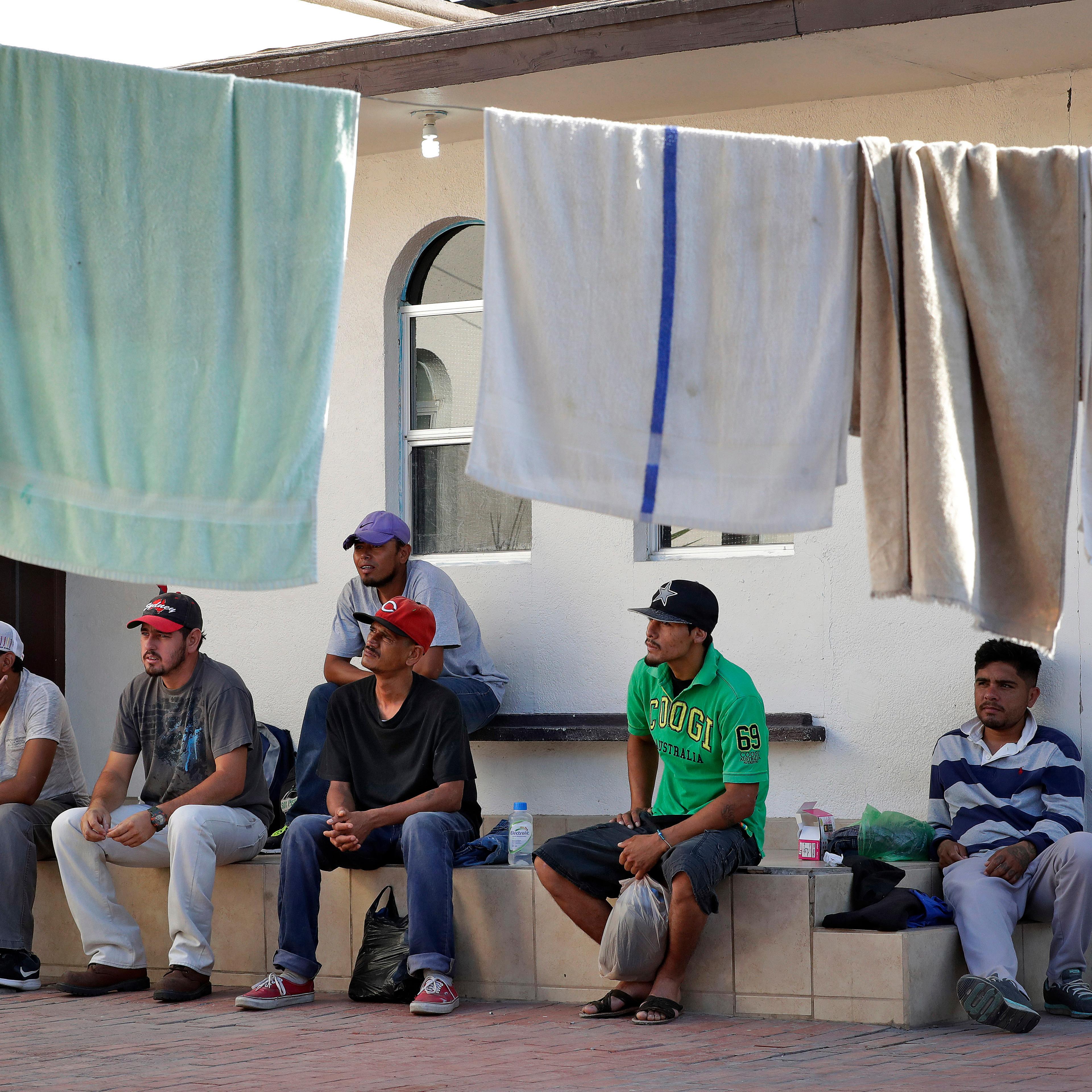 Men sit outside a home with laundry hanging to dry