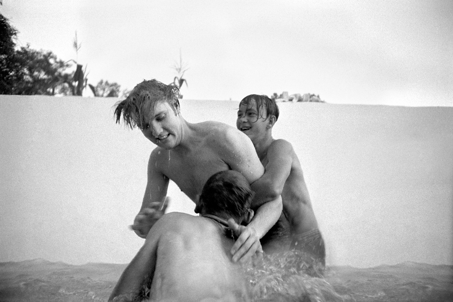 July 4, 1956. 1034 Auburn Drive, Memphis. Elvis liked horseplay — he loved physical activity. Here he is with his cousins Billy Smith (behind) and Bobby Smith (foreground) horsing around in a half-filled swimming pool at home. The valve was broken so they couldn't fill it all. I could stand on the solid base of the pool and shoot at their level.